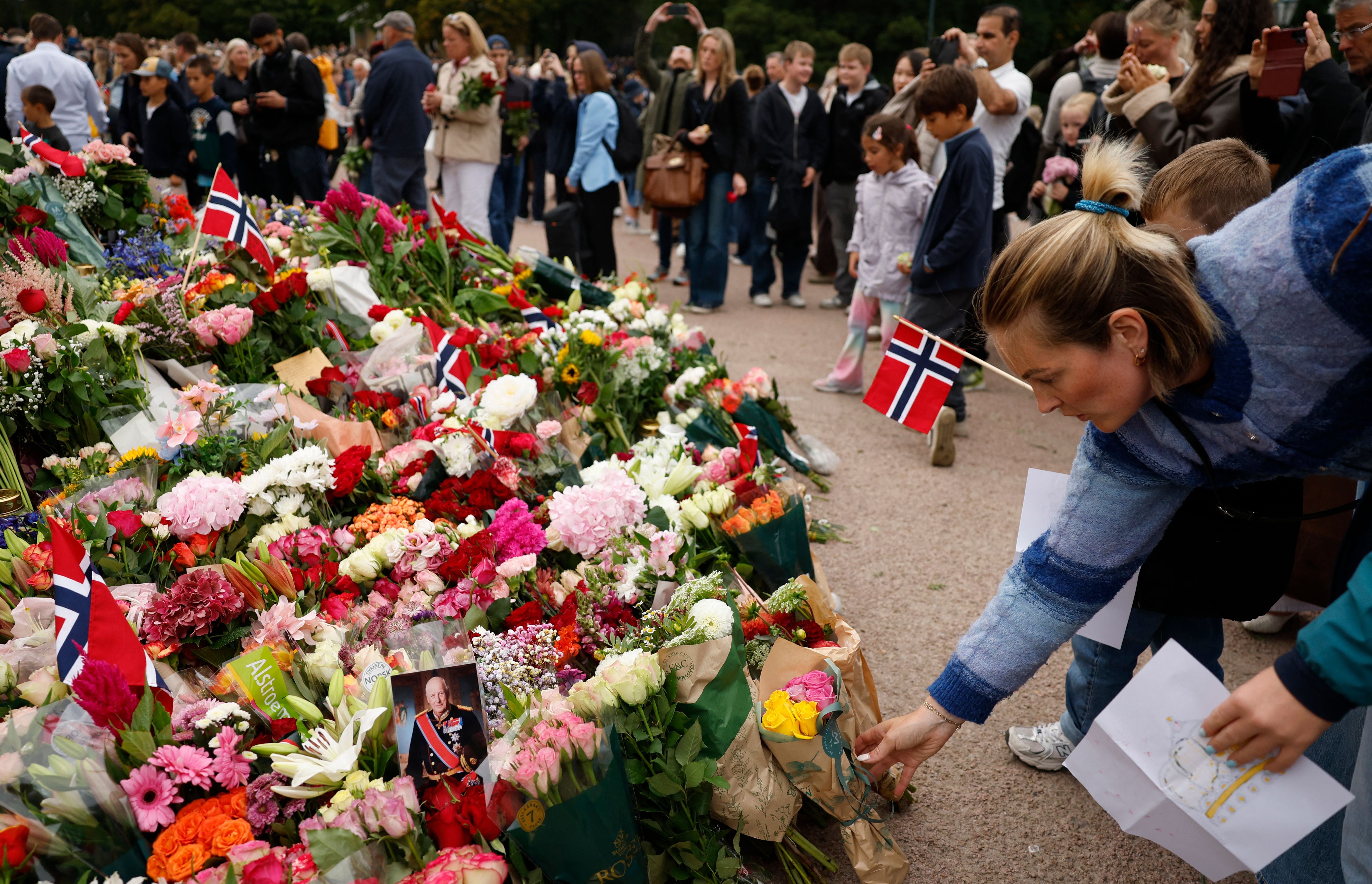 Viele Menschen legen Blumen und norwegische Flaggen an einem Gedenkort mit Foto von König Harald V. nieder.
