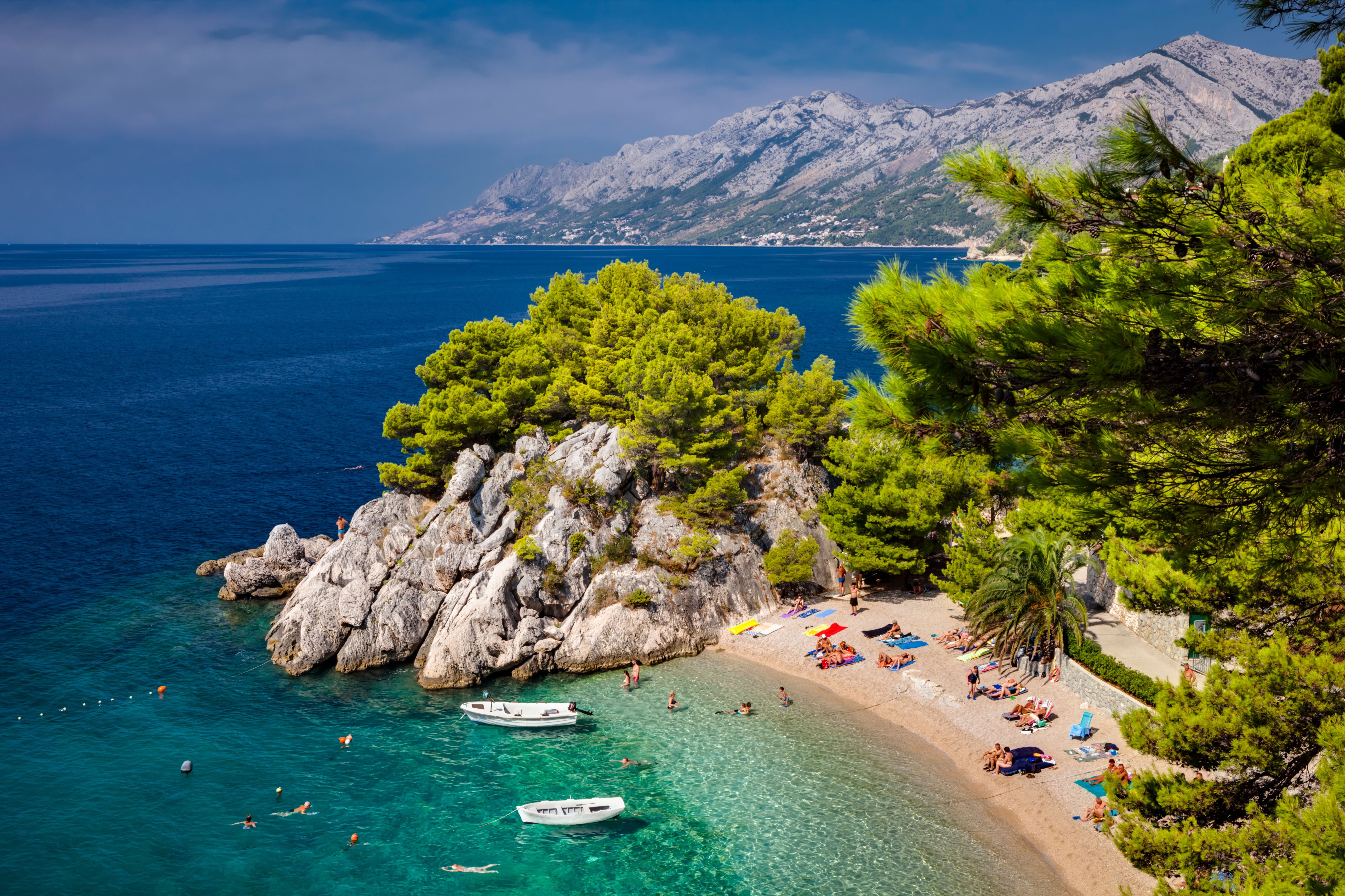 Sonniger Strand mit Badegästen, Pinienbäumen und klarem Wasser an der Makarska Riviera in Kroatien.