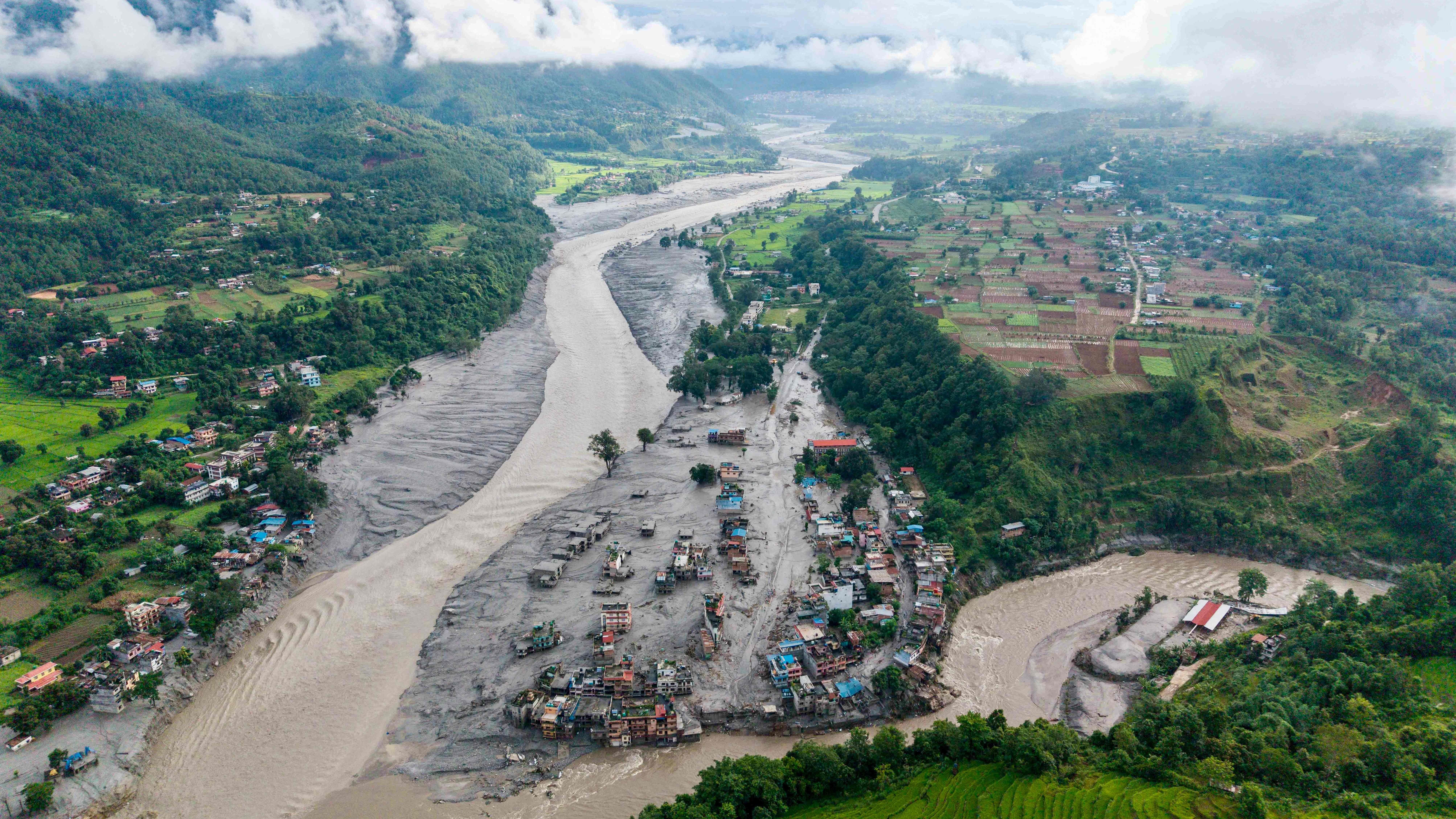 Luftaufnahme eines überfluteten Dorfes am Flussufer mit von Schlamm bedeckten Häusern in Nepal.