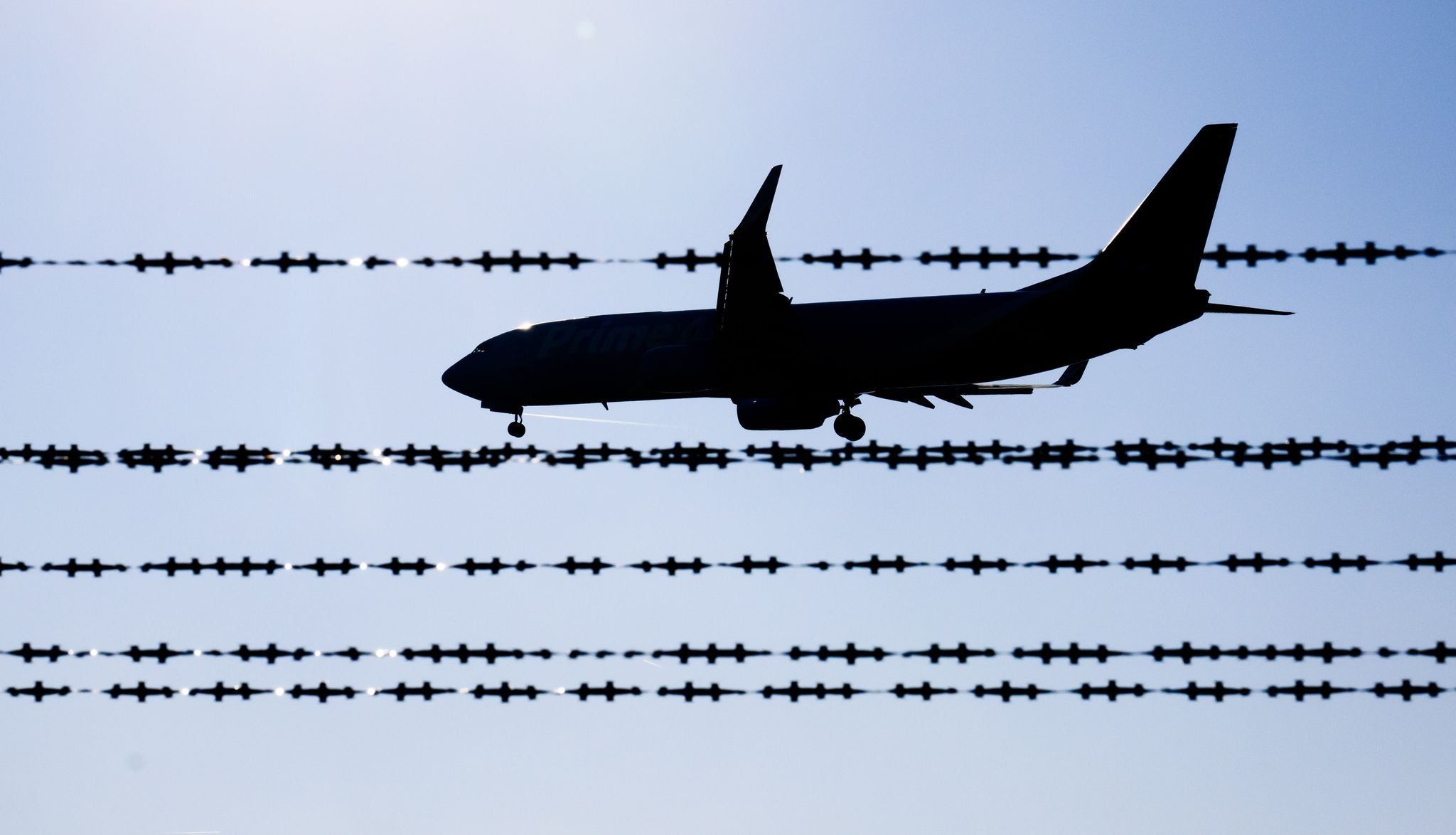 Ein Flugzeug fliegt hinter Stacheldraht vor blauem Himmel am Flughafen Hannover.