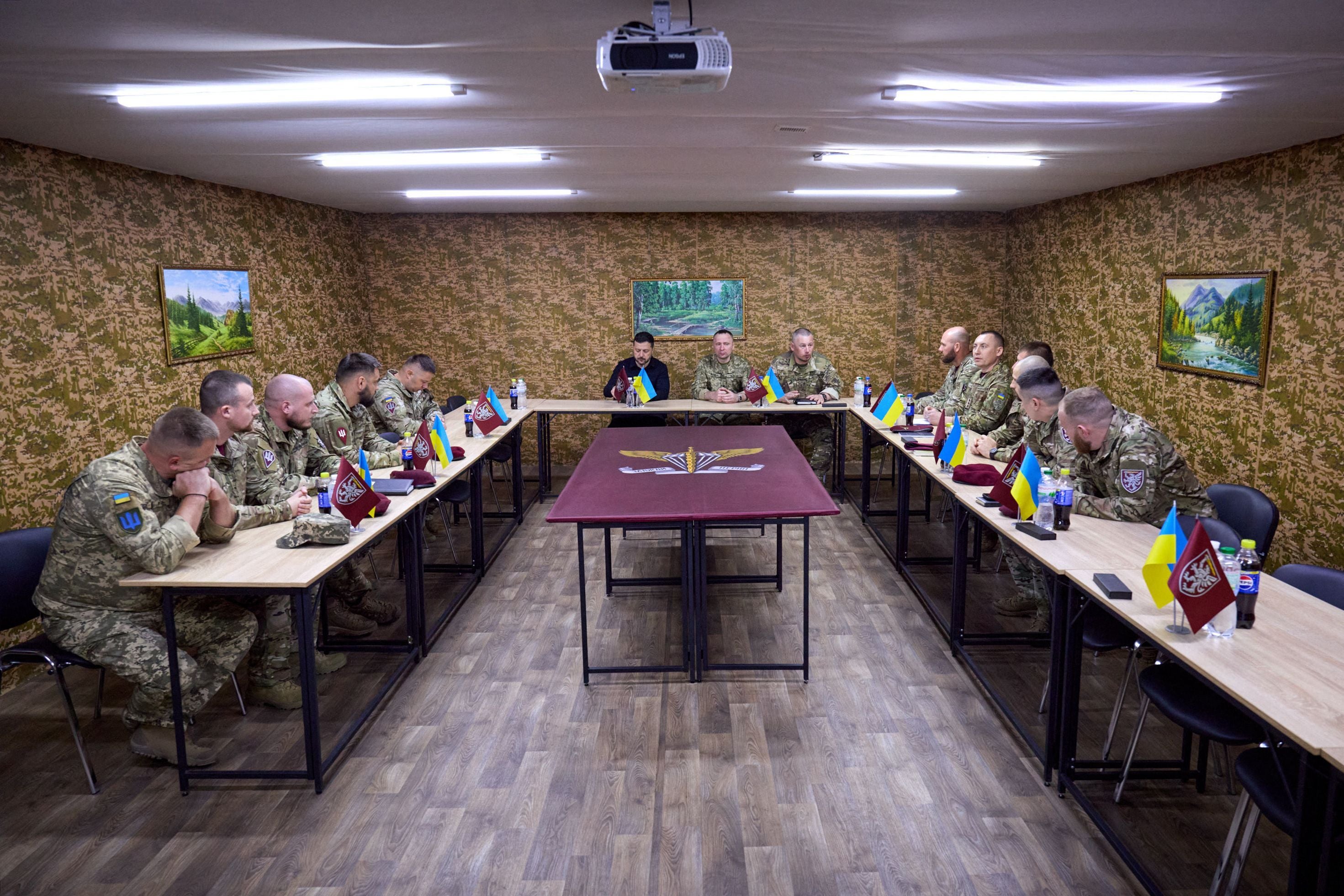 Der ukrainische Präsident Wolodymyr Selenskyj, ukrainische Soldaten und Offiziere sitzen in Uniformen um einen Konferenztisch.