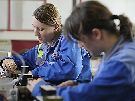 Zwei junge Frauen arbeiten in blauen Arbeitsjacken an technischen Geräten.