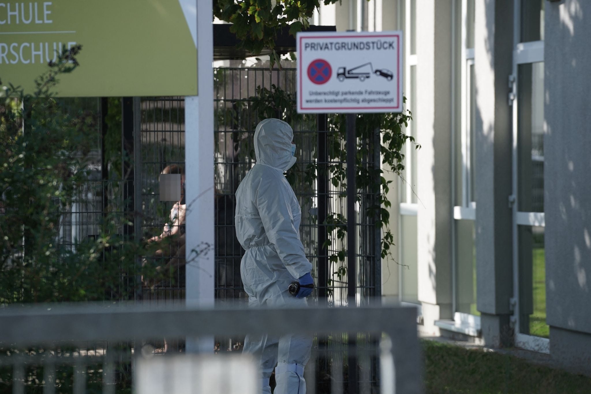 Eine Person im weißen Schutzanzug steht vor einem Gebäude mit Privatgrundstück-Schild.