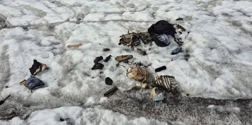 Verschiedene Kleidung und Gegenstände liegen verstreut auf Schnee und Eis.