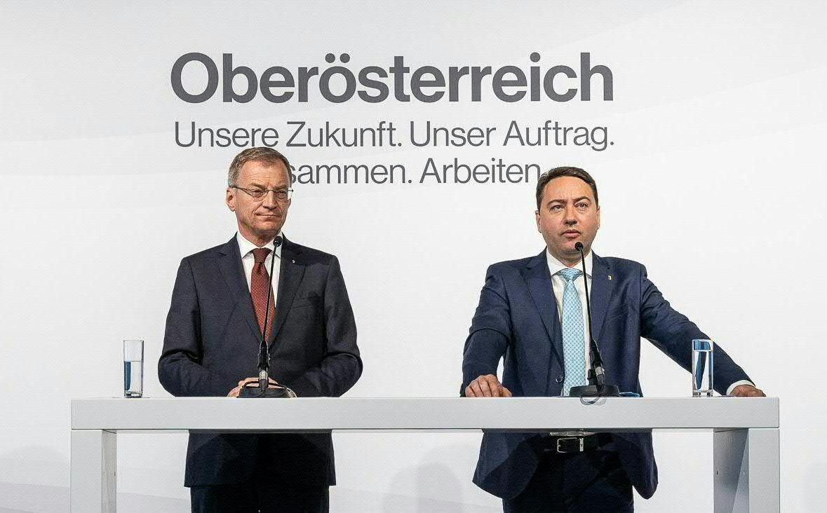 Zwei Männer im Anzug stehen an einem Rednerpult vor der Aufschrift "Oberösterreich".