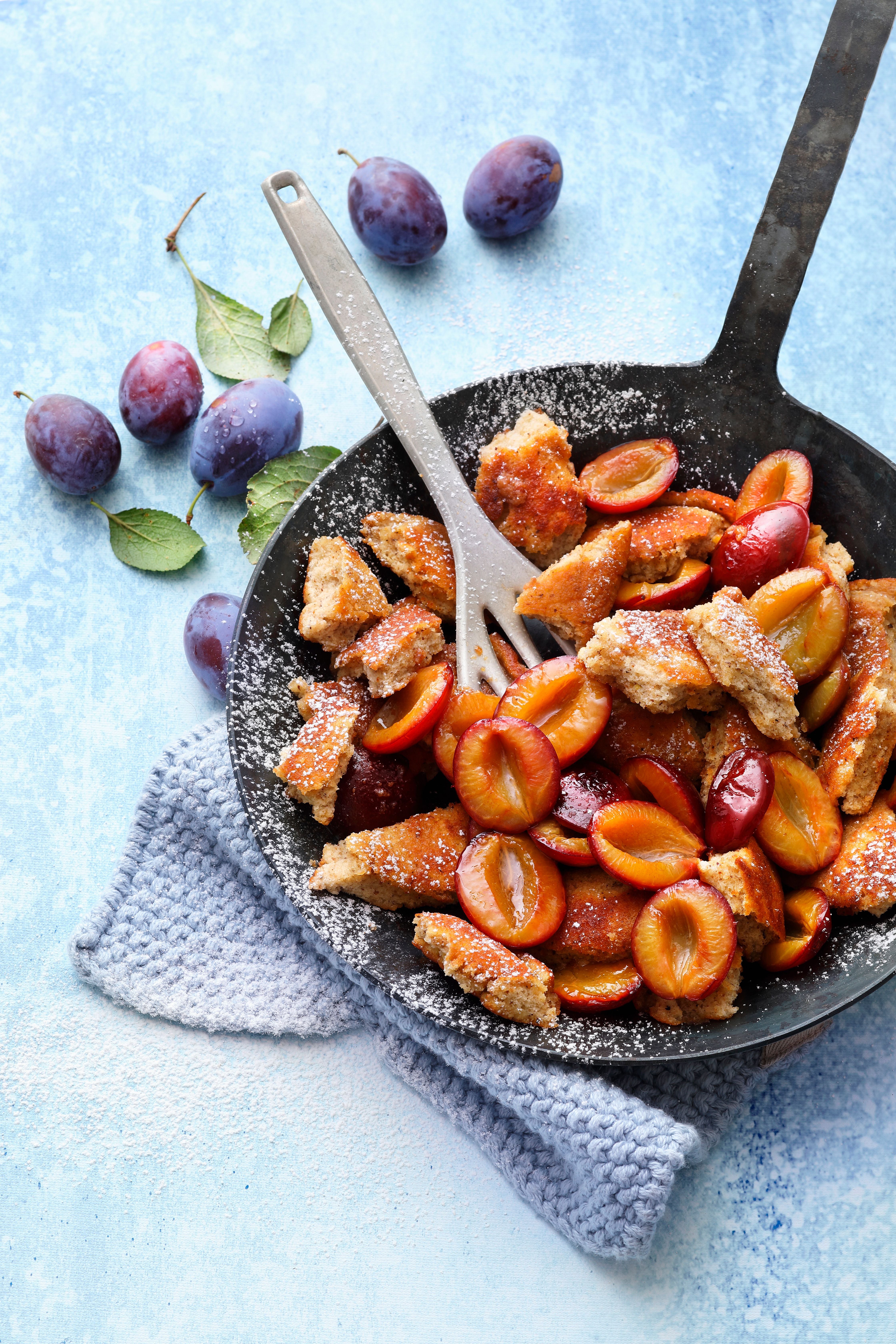 Pfanne mit Haselnuss-Schmarrn und frischen Zwetschgen, bestreut mit Puderzucker.