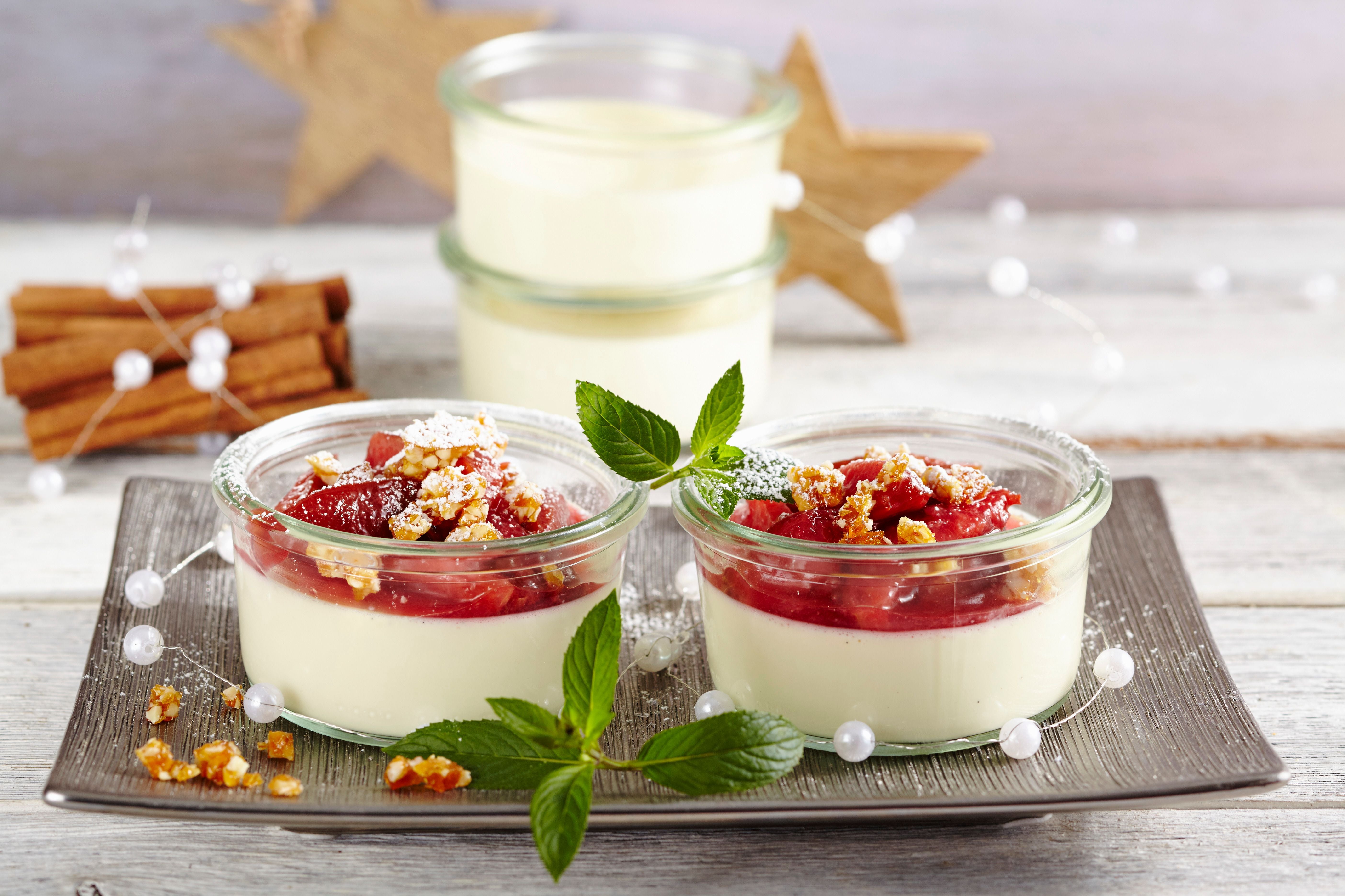 Panna Cotta mit Zimt-Zwetschgen, Mandelkrokant und Minze im Weckglas auf einem Teller.