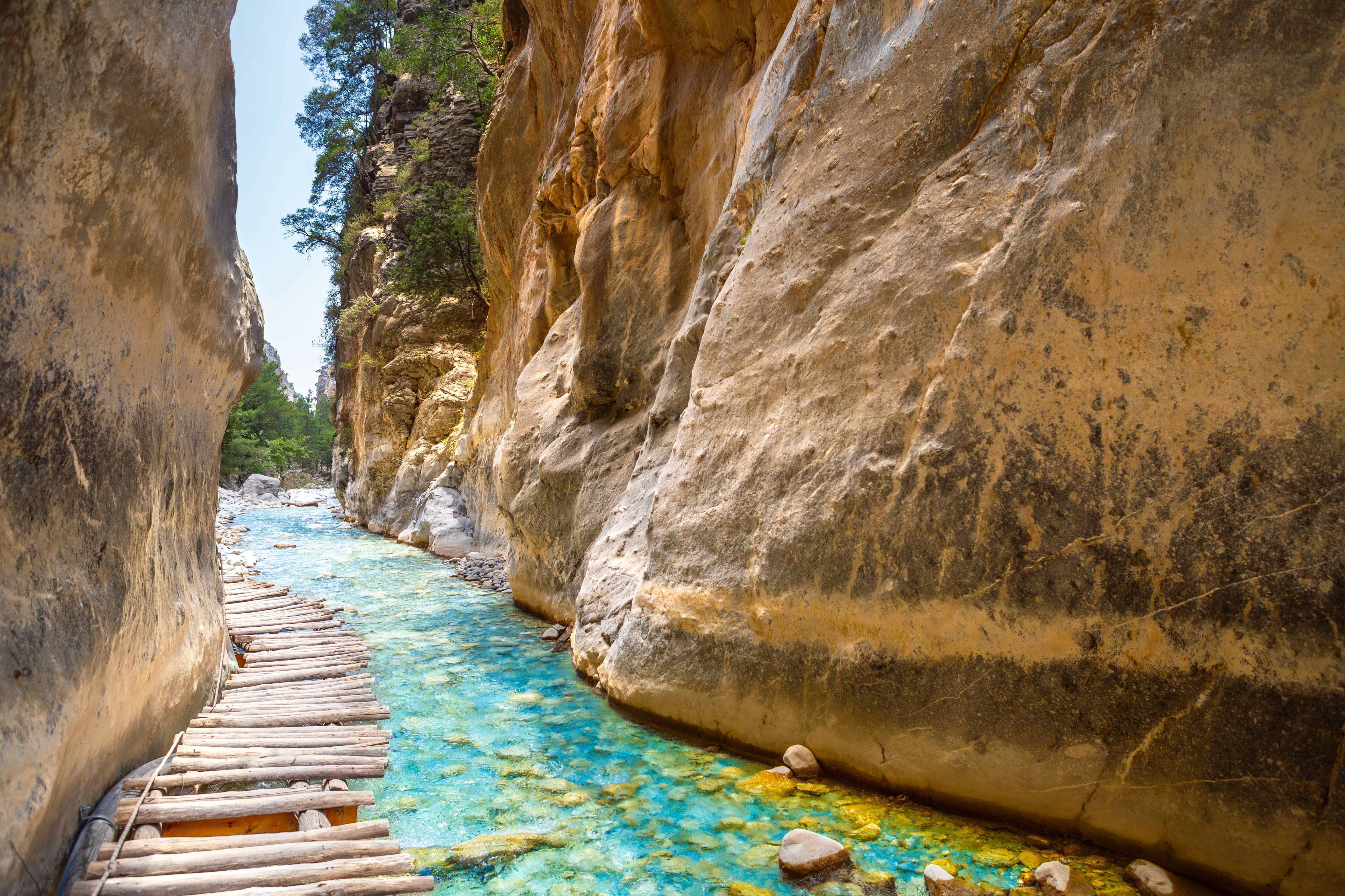 Schmale Holzbrücke führt durch die felsige Samaria-Schlucht mit türkisfarbenem Wasser auf Kreta.