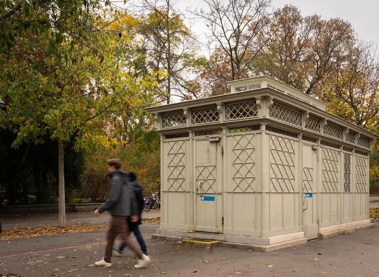 Zwei Personen gehen an einer öffentlichen Toilette am Wiener Parkring vorbei.