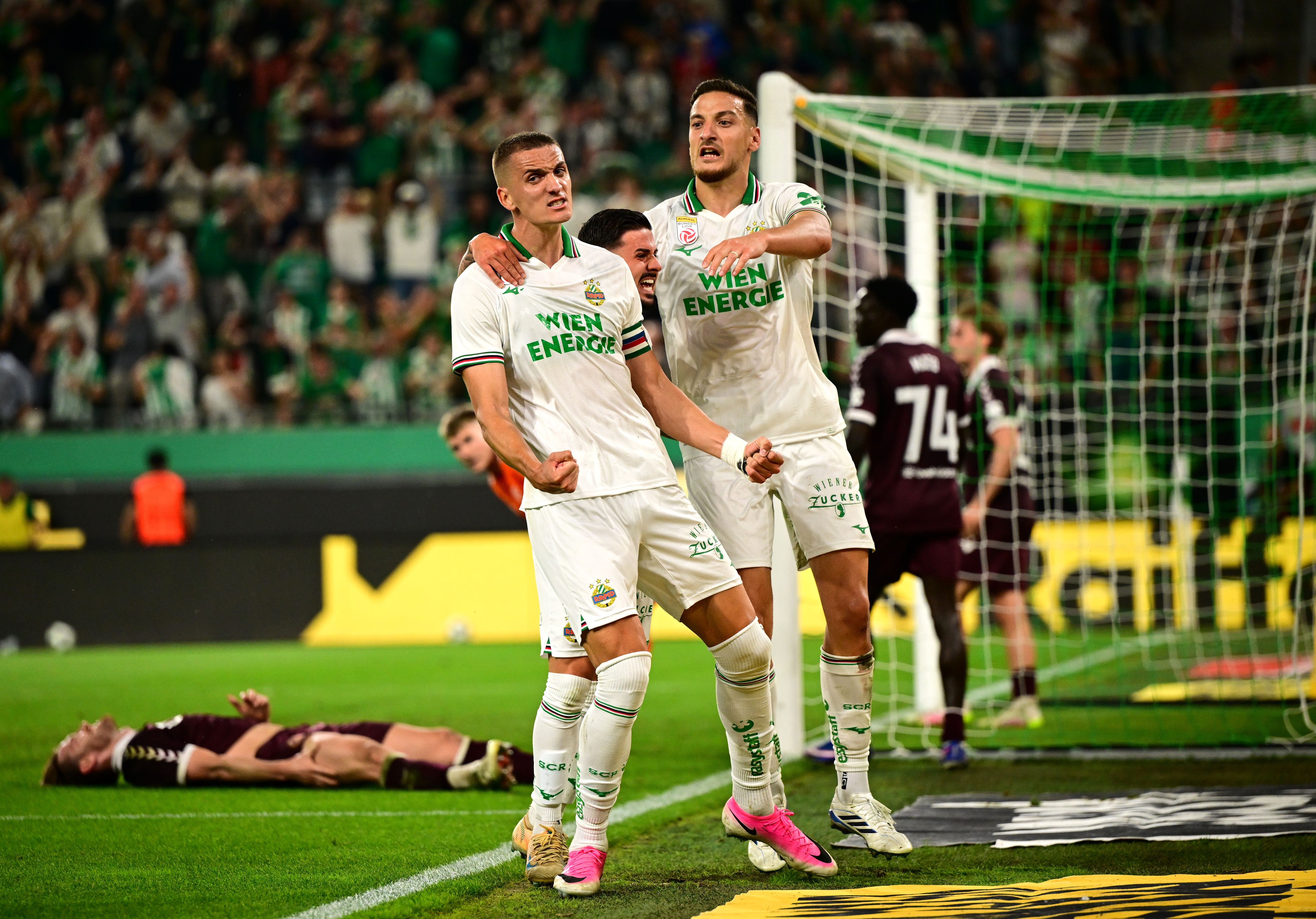 Rapid-Wien-Spieler jubeln nach einem Tor vor dem Tor, ein Gegner liegt am Boden.