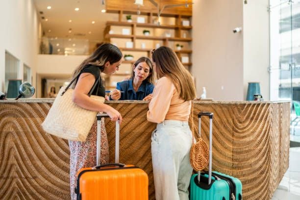 Zwei Frauen mit Koffern sprechen mit einer Rezeptionistin an einem Hotel-Lobbytresen.