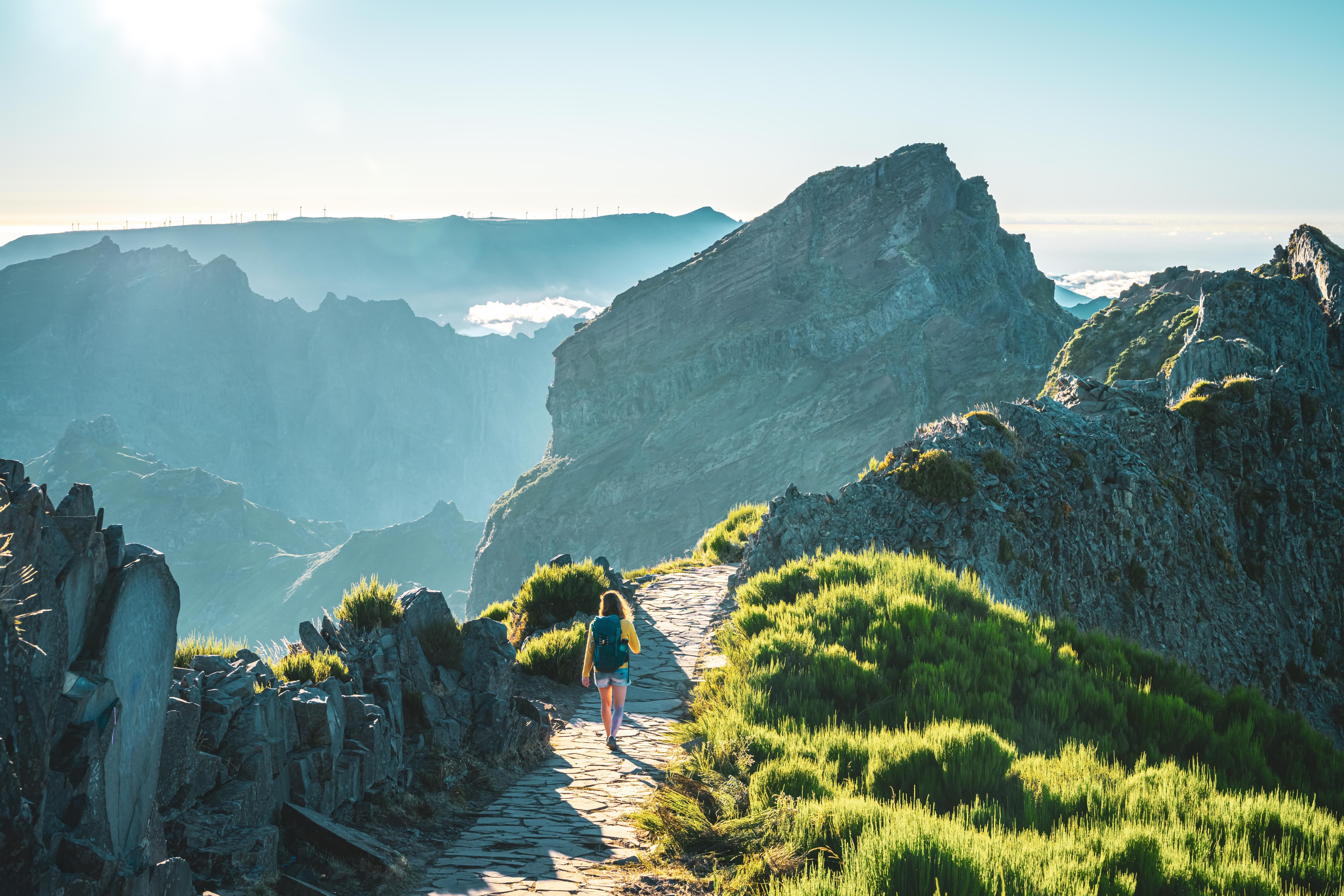 Frau wandert am Abend auf steinigem Bergpfad zwischen grünen Hügeln und Felsen auf Madeira.