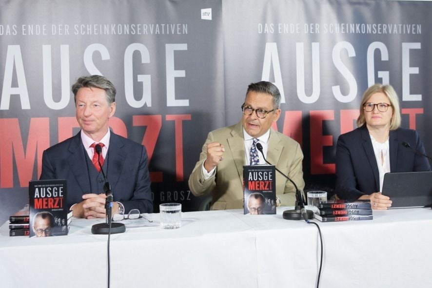 Drei Personen sitzen bei einer Buchvorstellung mit dem Titel "Ausgemerzt" an einem Tisch.