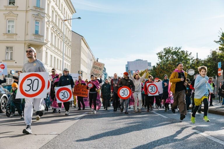Demonstrierende halten Tempo-30-Schilder auf einer Straße in einer Stadt.