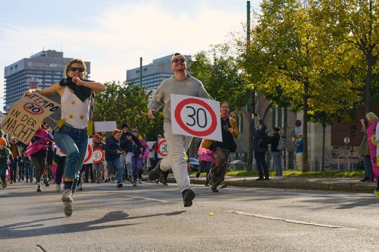 Menschen laufen bei einer Demonstration auf der Straße und halten Tempo-30-Schilder hoch.
