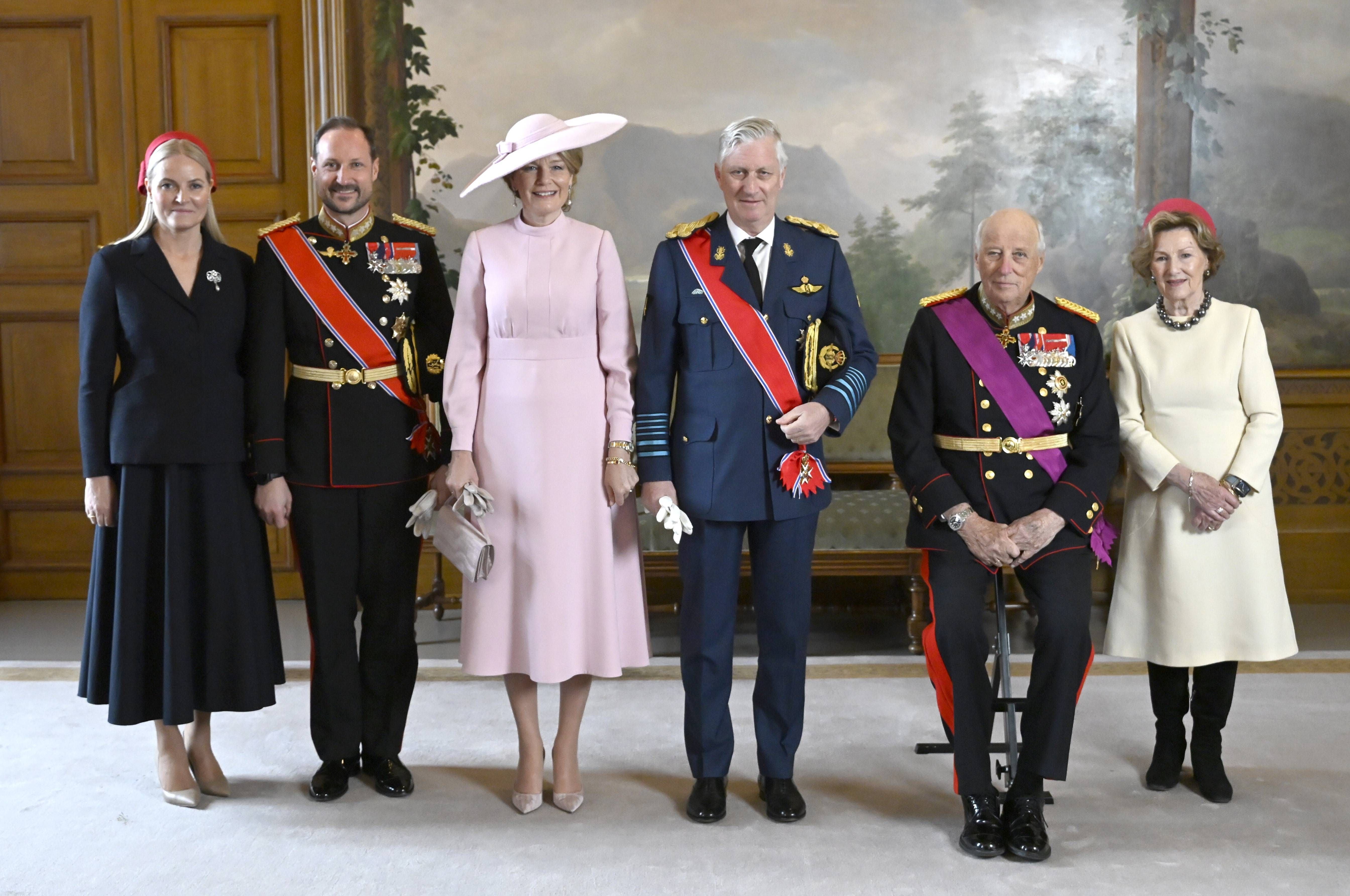 Sechs elegant gekleidete Personen posieren für ein offizielles Gruppenfoto in einem prunkvollen Raum.