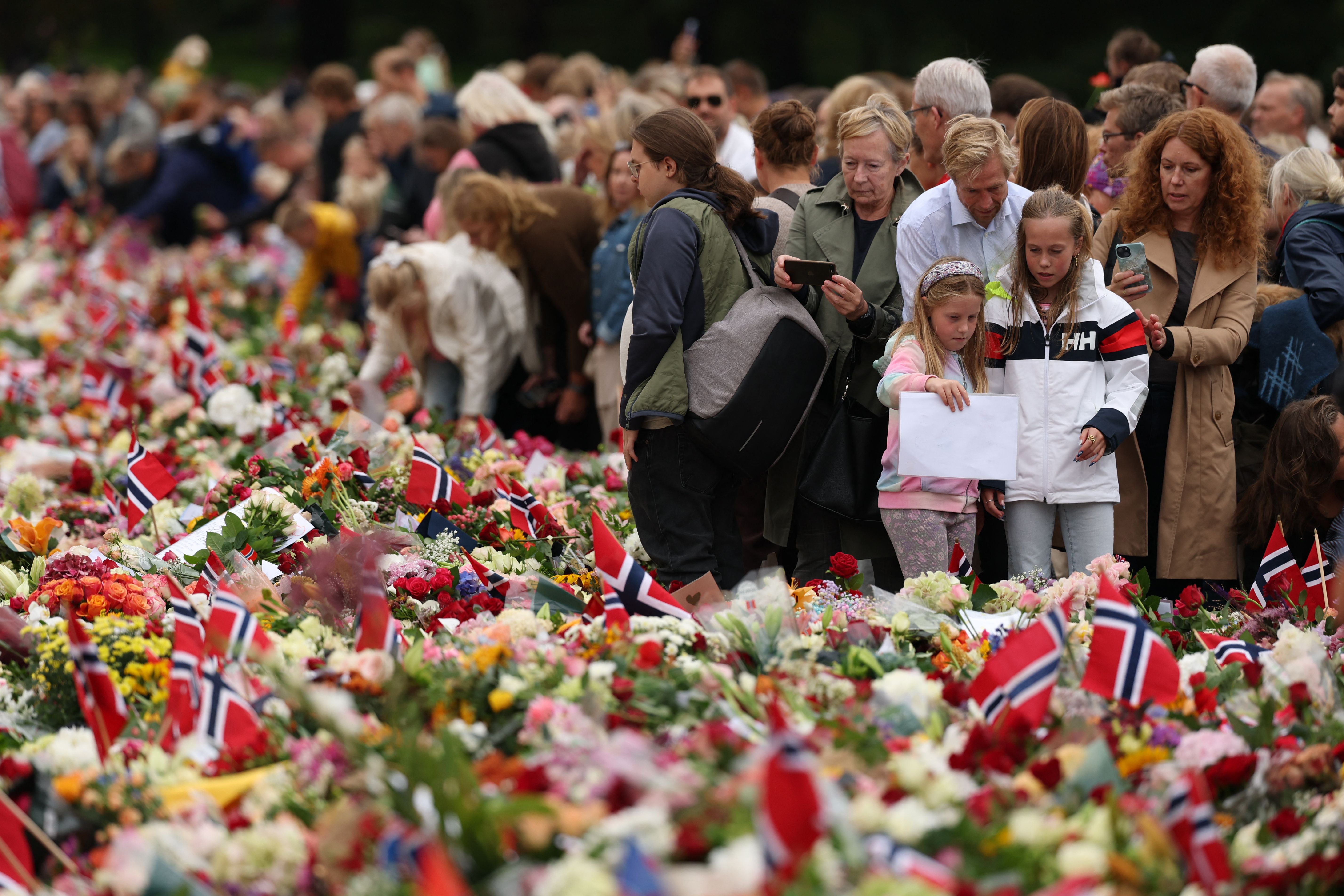 Viele Menschen trauern an einem Blumenmeer mit norwegischen Flaggen vor dem Königspalast in Oslo.