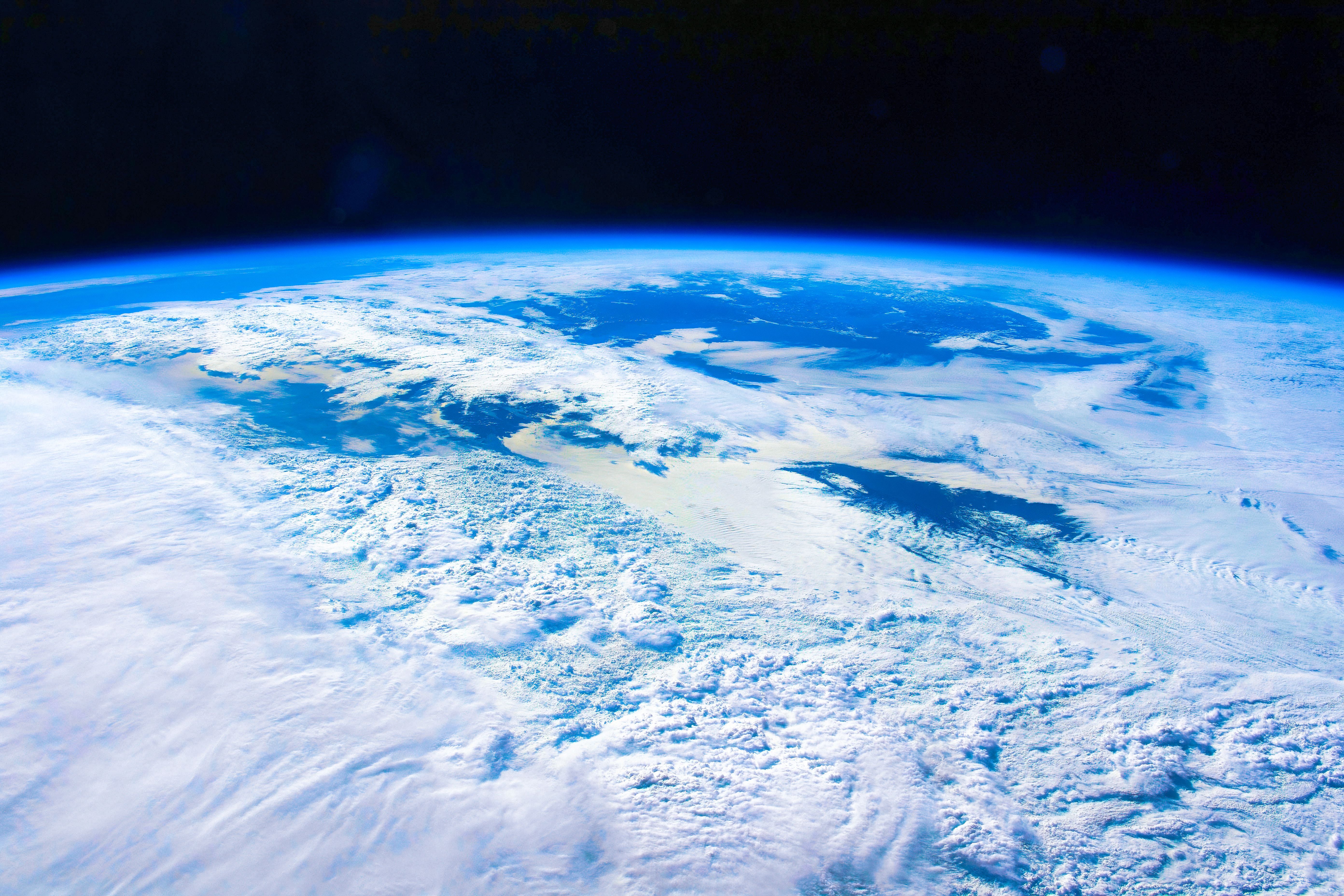 Blick aus dem All auf die Erde mit Wolkenfeldern und einer leuchtend blauen Atmosphäre.