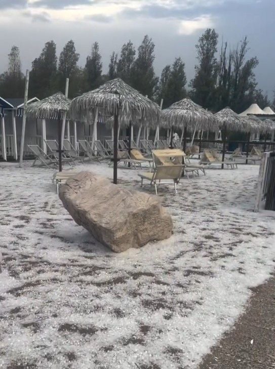 Hagelkörner bedecken einen Strand mit Sonnenliegen und Strohdächern an der Adria.