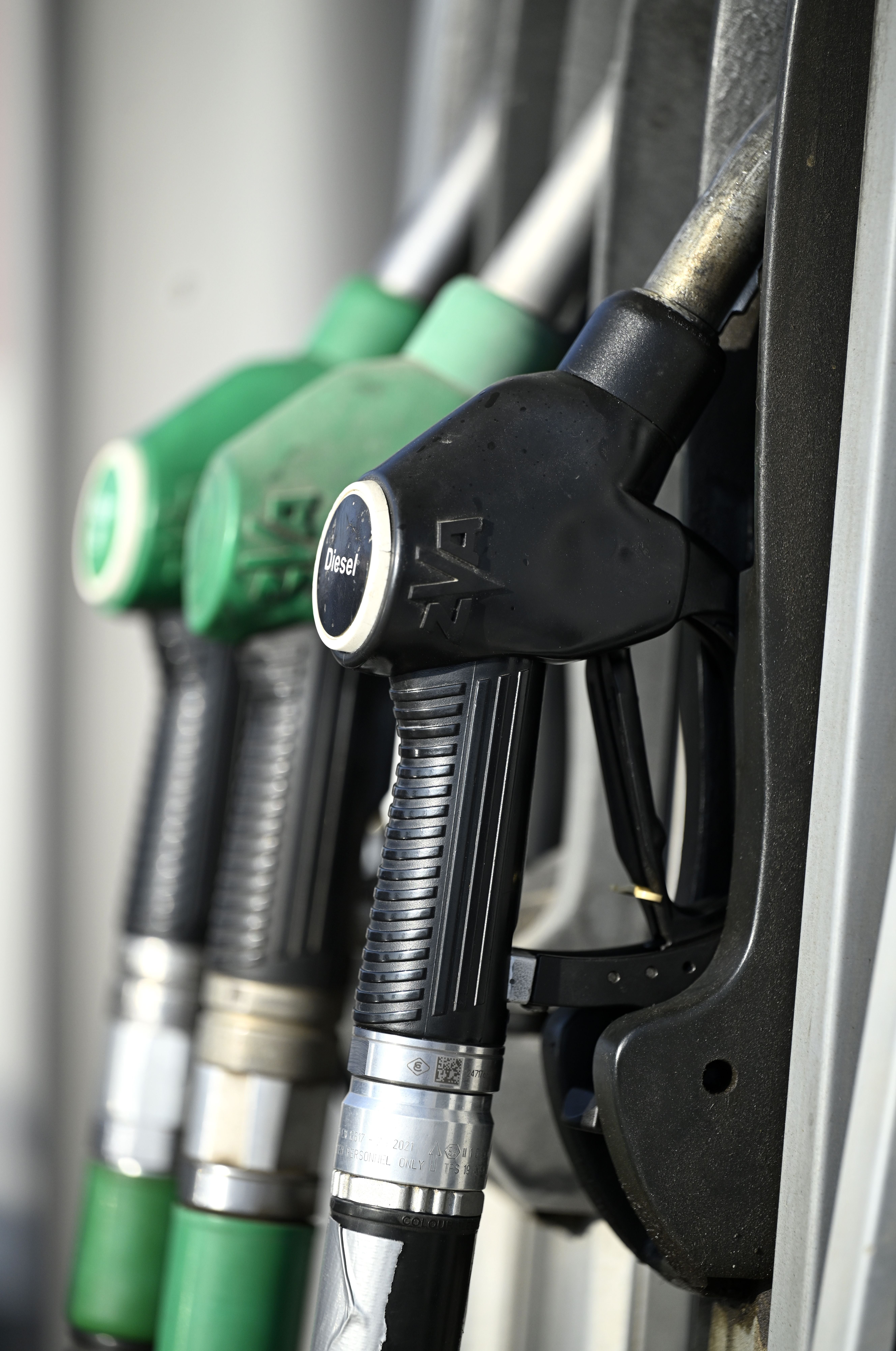 Zapfpistolen an einer Tankstelle, vorne eine schwarze Dieselpistole, dahinter grüne Benzinpistolen.