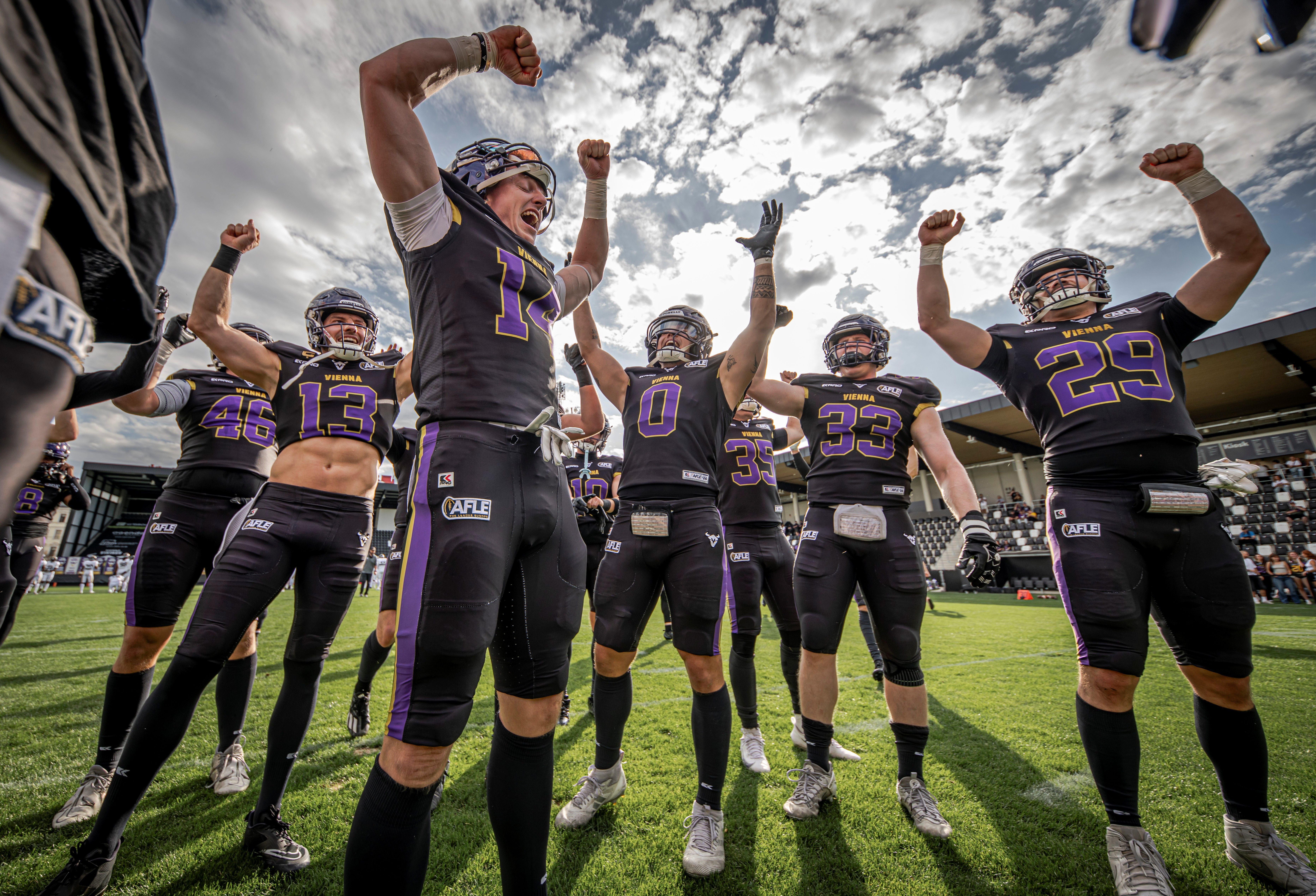 Mehrere Footballspieler der Vienna Vikings jubeln mit erhobenen Armen auf dem Spielfeld.