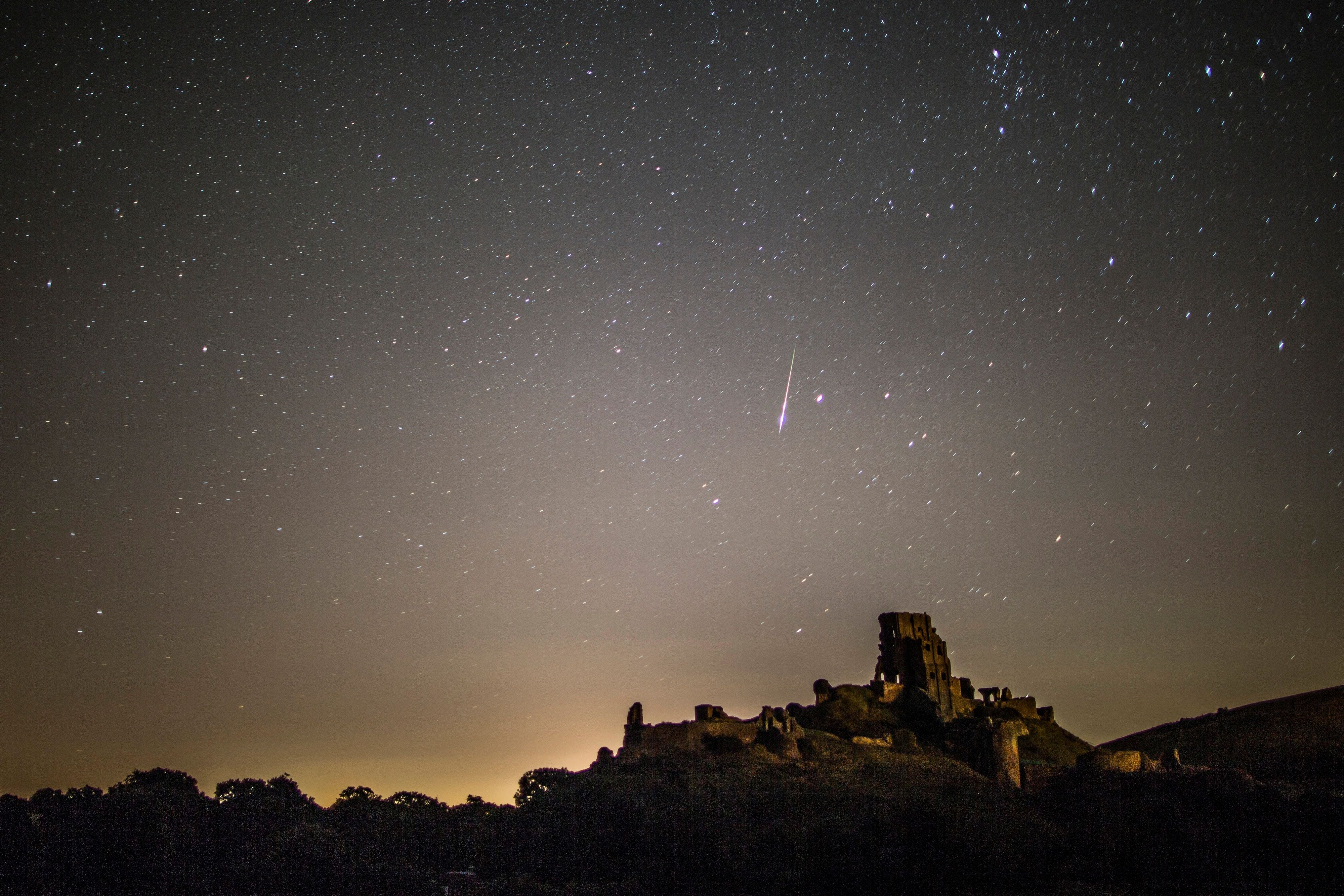 Ruine von Corfe Castle unter sternenklarem Himmel mit hellen Perseiden-Meteor im August.