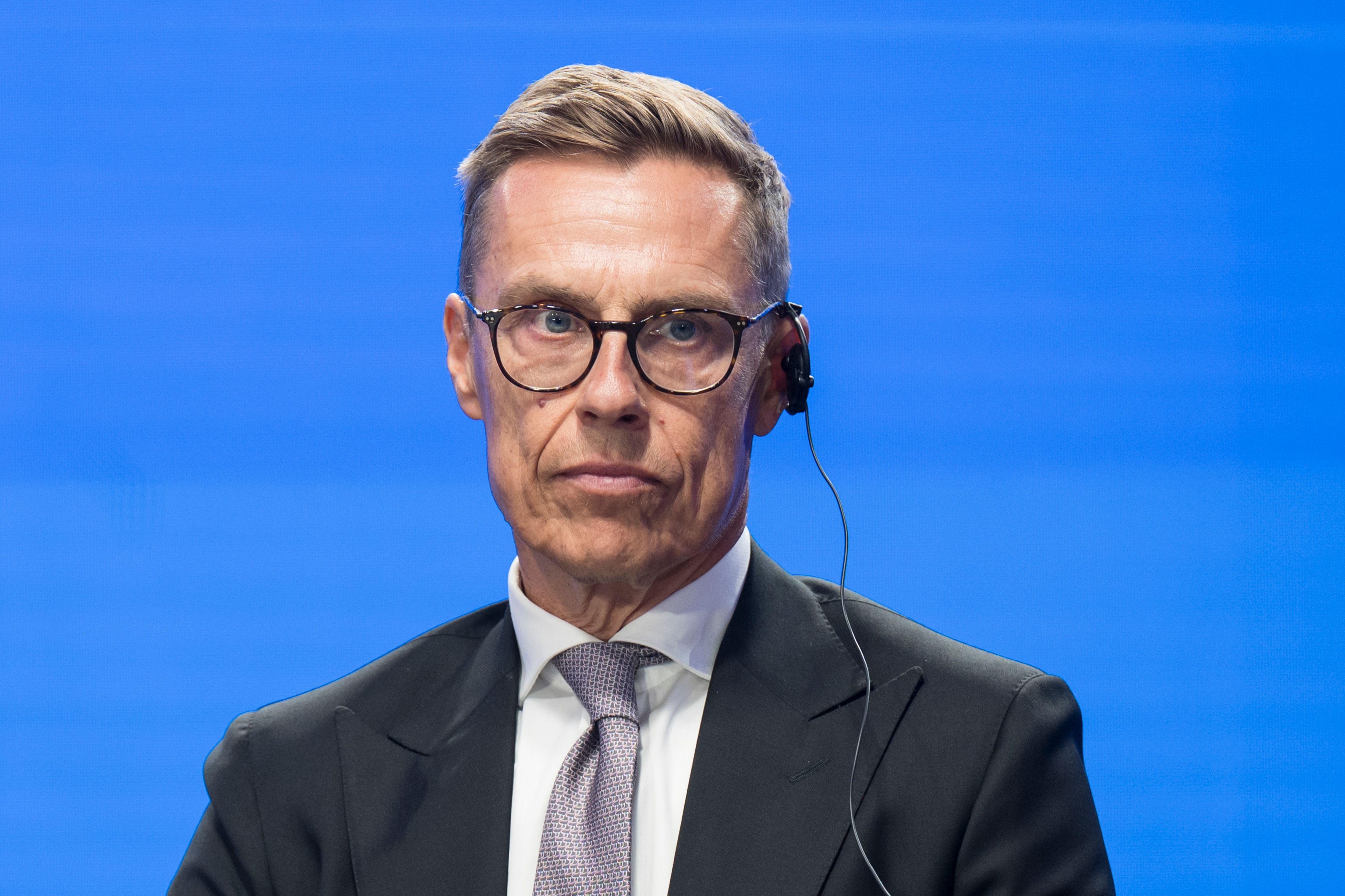 Ein Mann im Anzug mit Brille und Headset vor blauem Hintergrund.