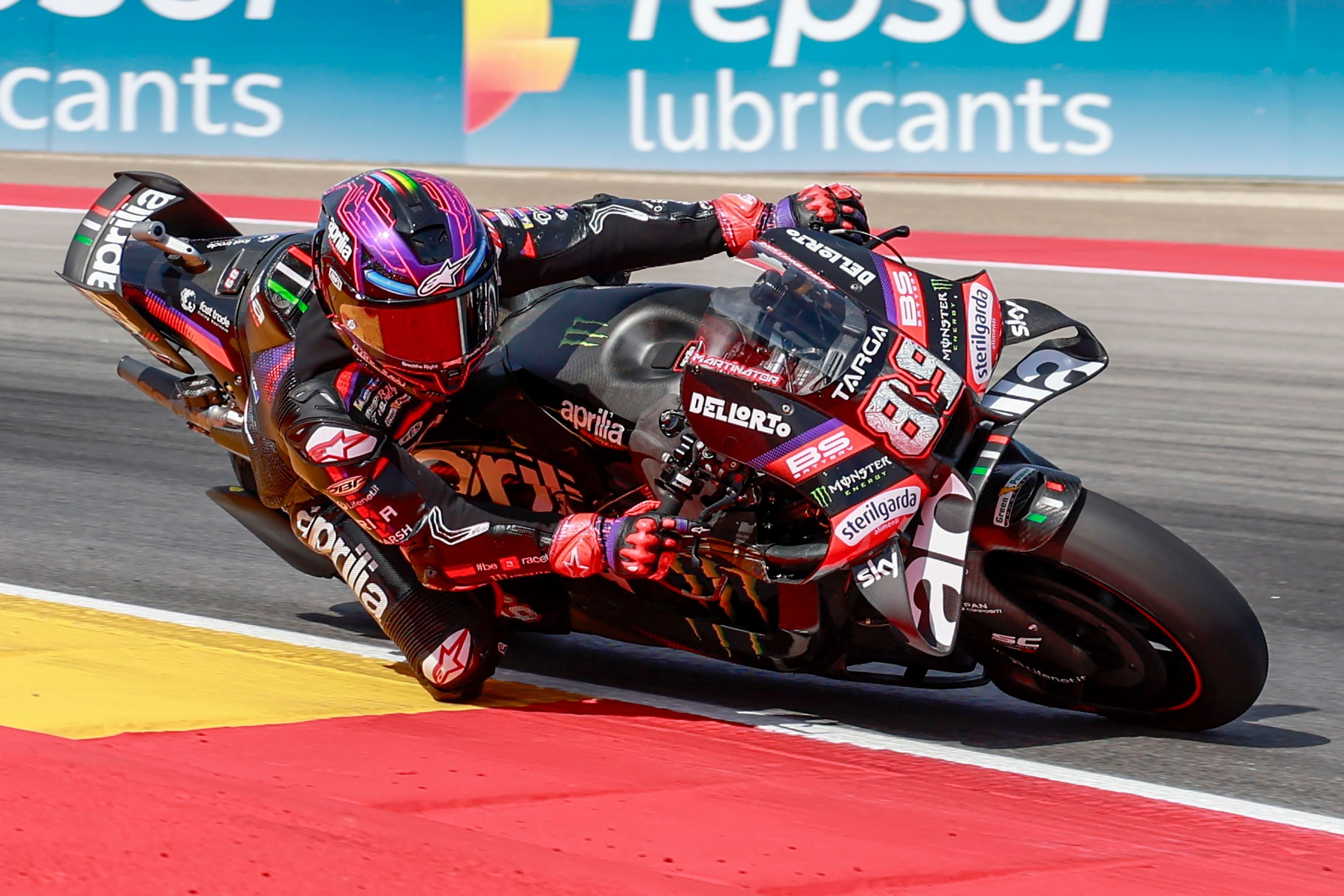 Motorradrennfahrer Jorge Martin mit einem bunt schimmernden Helm und Lederkombi lehnt sich auf einem schwarzen Aprilia-Renner tief in eine Rechtskurve auf der Rennstrecke.