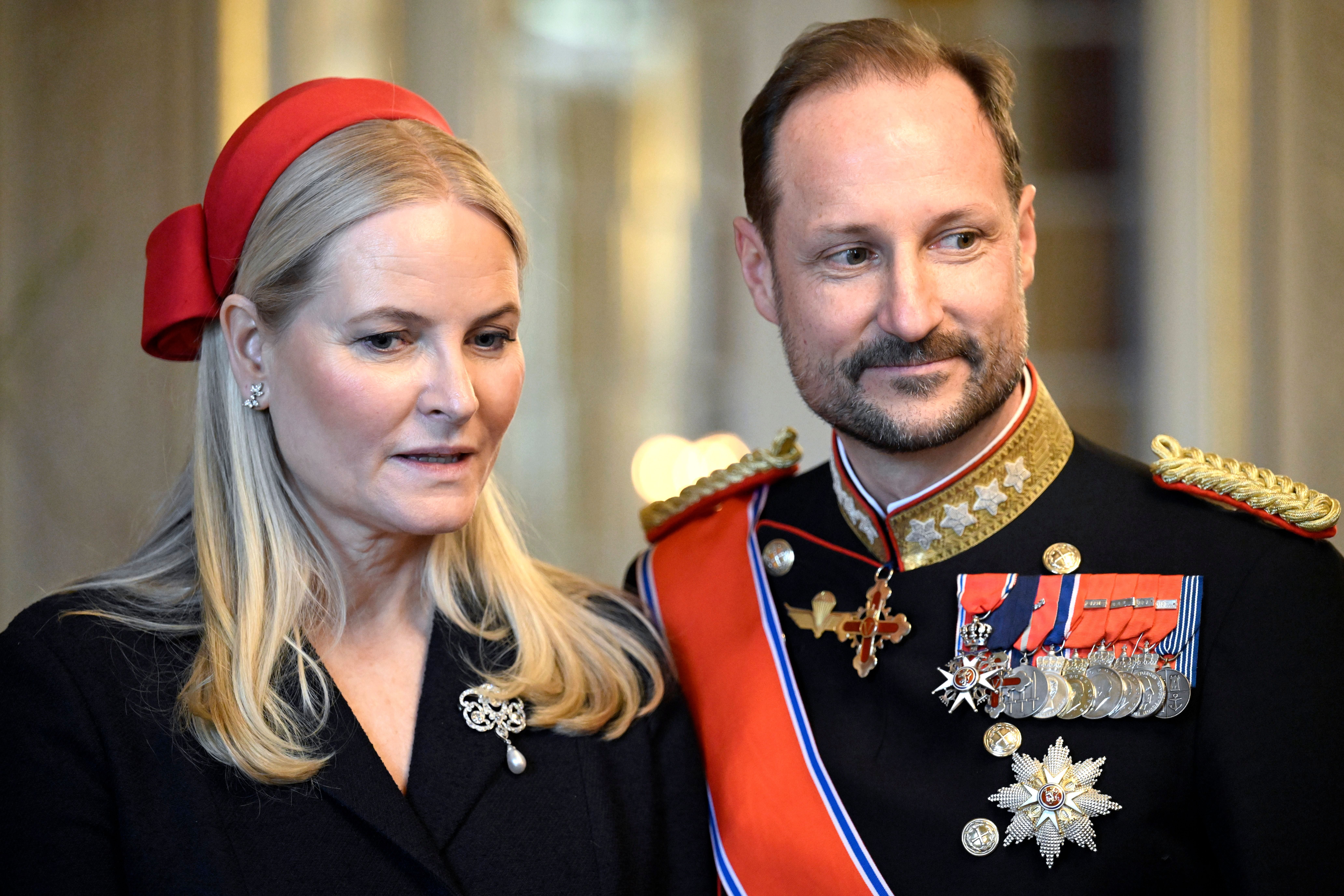 Ein Paar in formeller Kleidung posiert, er trägt Uniform mit Orden, sie ein rotes Haarband.