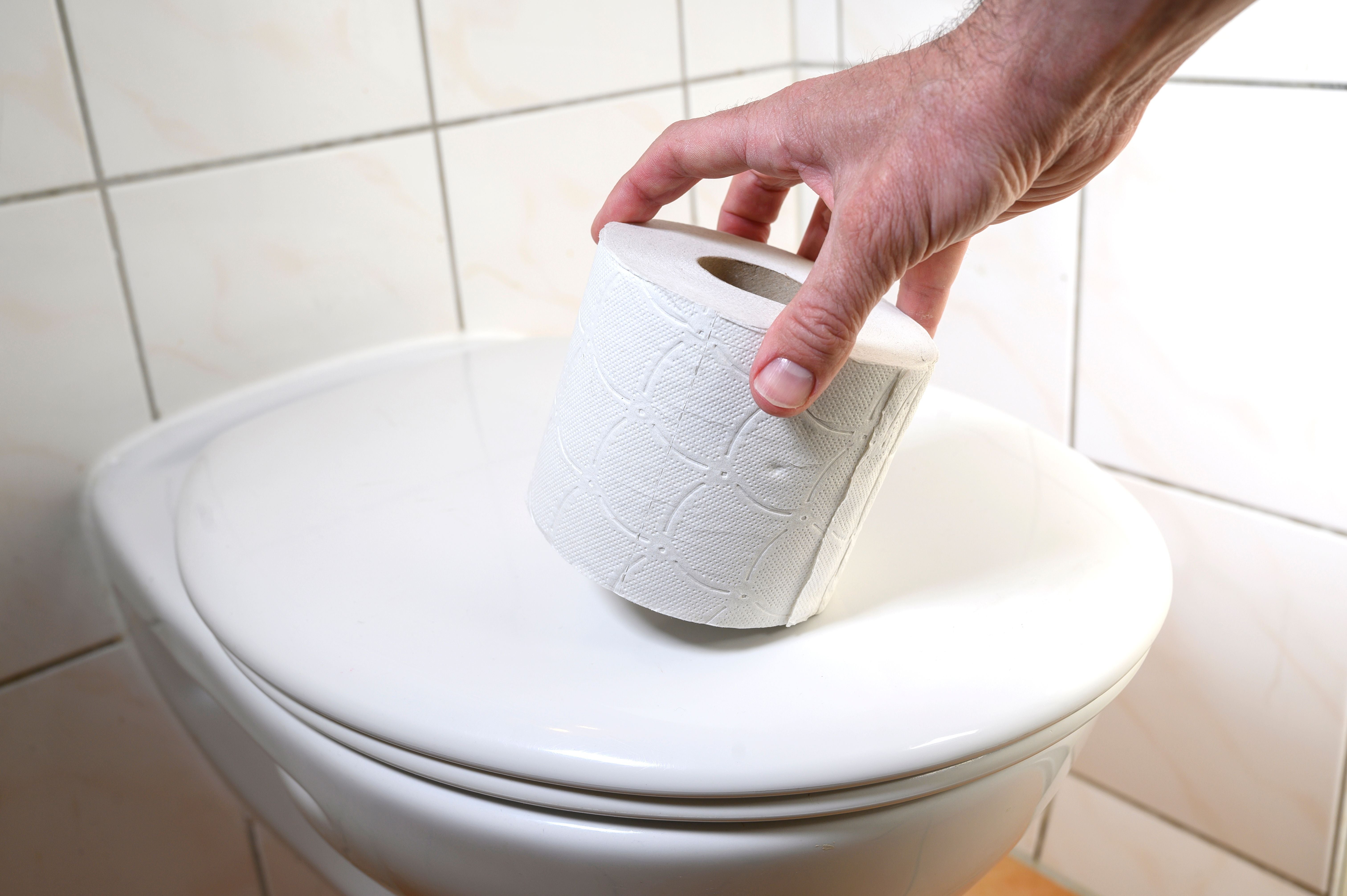 Hand legt eine Toilettenpapierrolle auf einen geschlossenen Toilettendeckel.