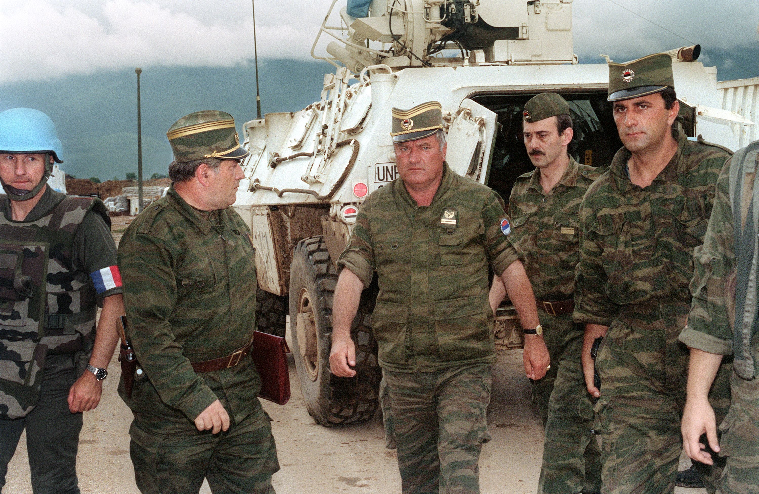 Mehrere Soldaten in Uniform gehen vor einem gepanzerten Fahrzeug, ein UN-Soldat links im Bild.