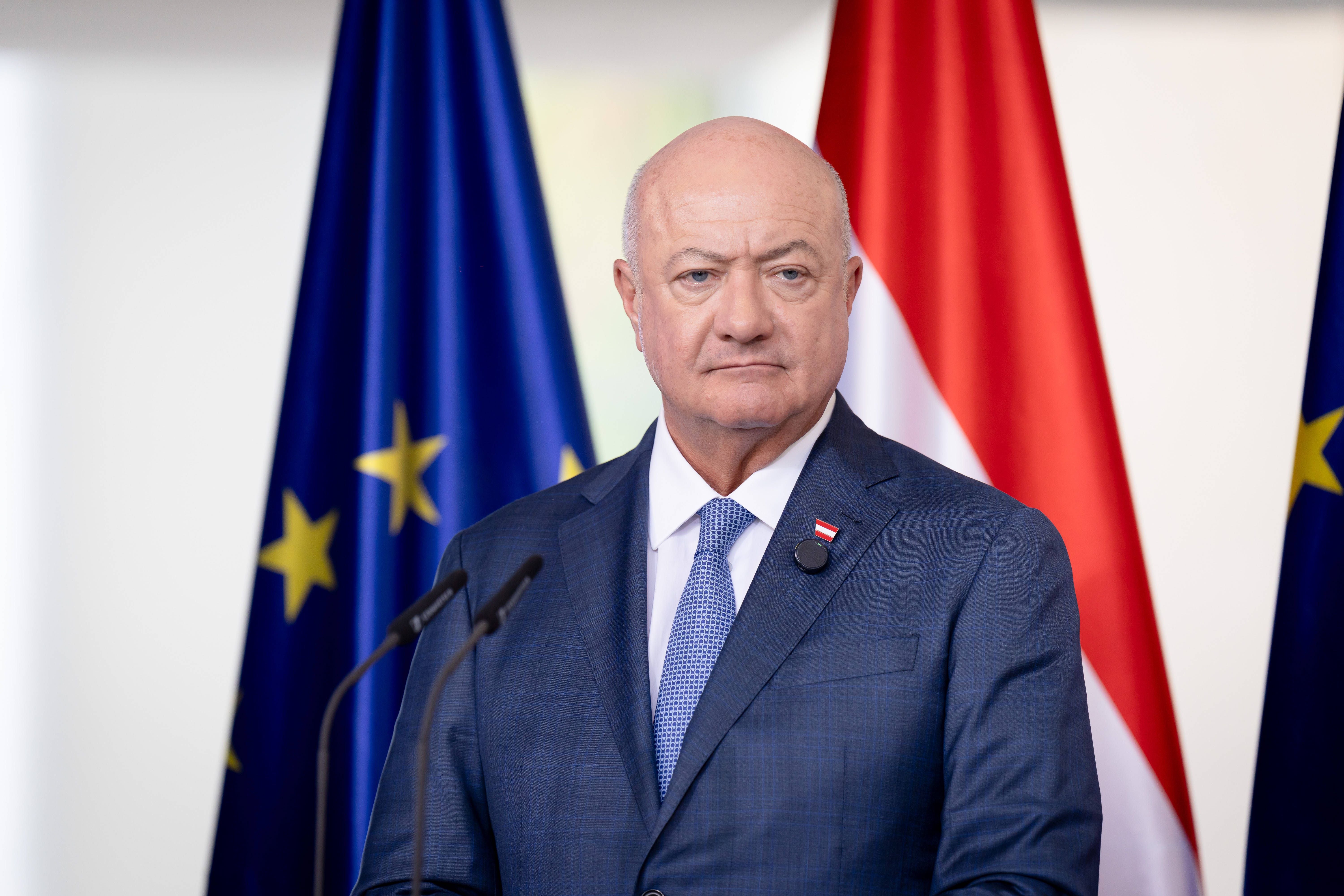 Ein Mann im Anzug steht vor EU- und Österreich-Flaggen bei einer Pressekonferenz.