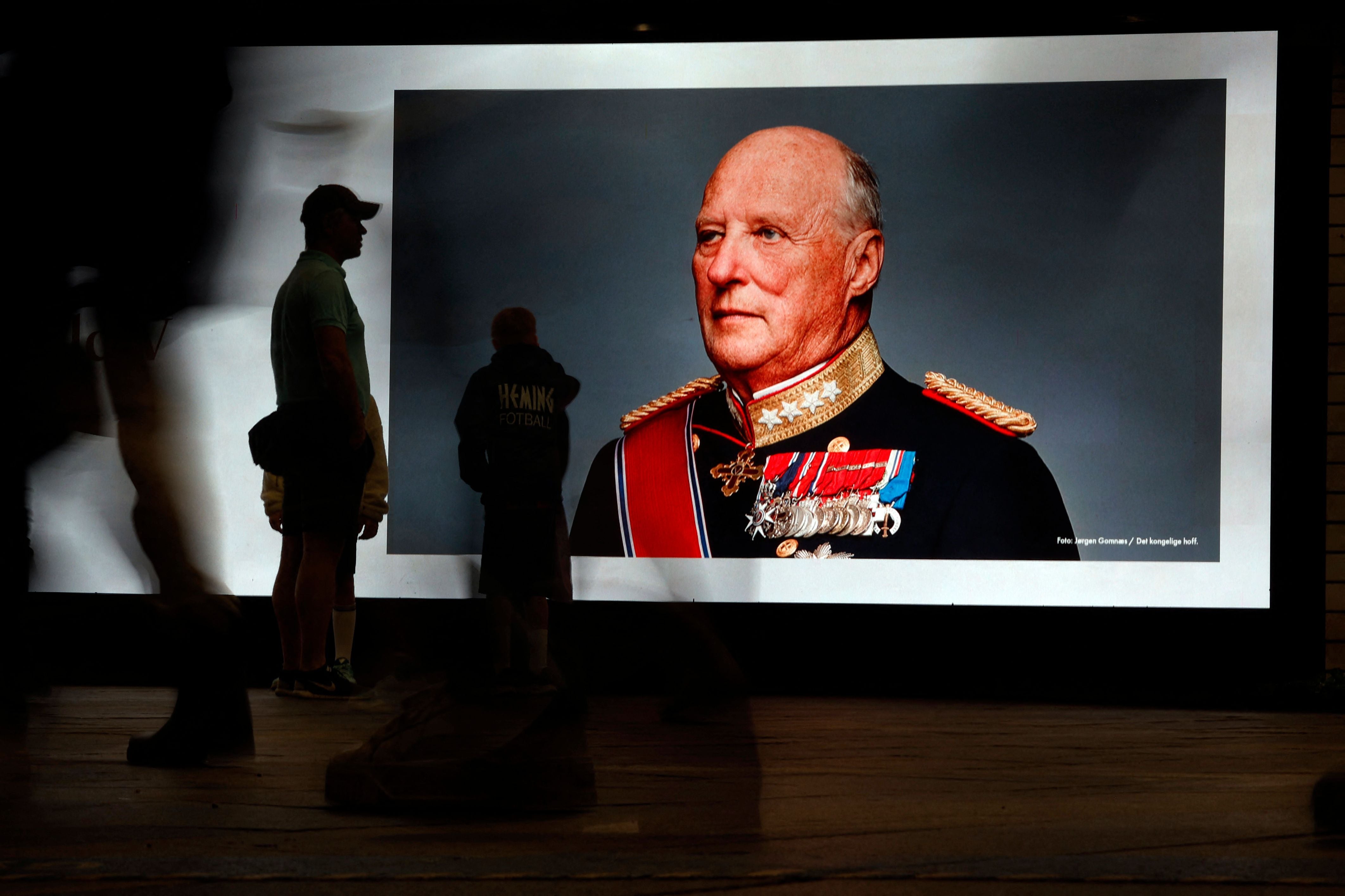 Menschen betrachten ein großes Gedenkporträt von Norwegens König Harald V. an einer Wand.