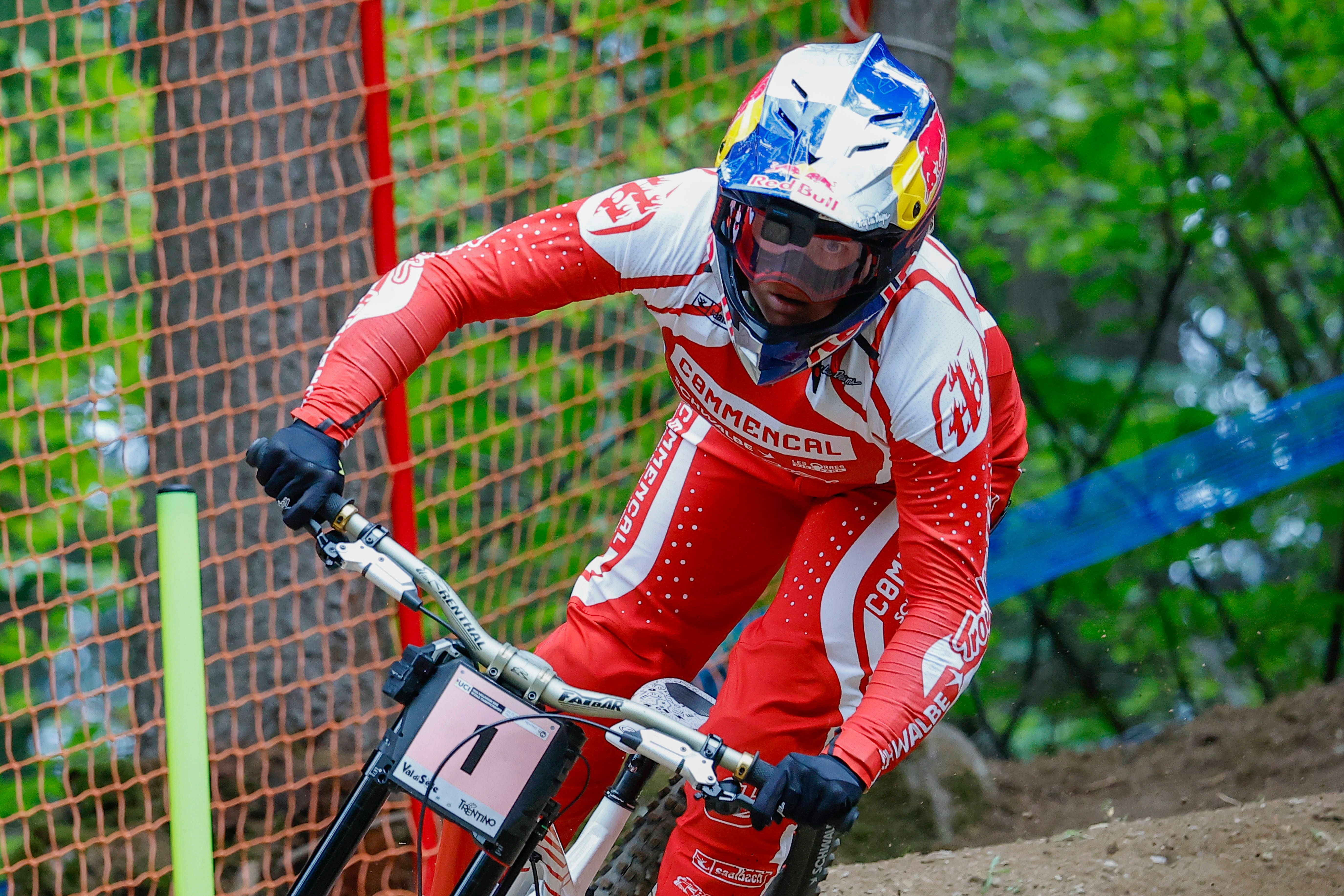 Mountainbikerin in rotem Rennanzug fährt mit Helm und Brille eine Downhill-Strecke im Wald.
