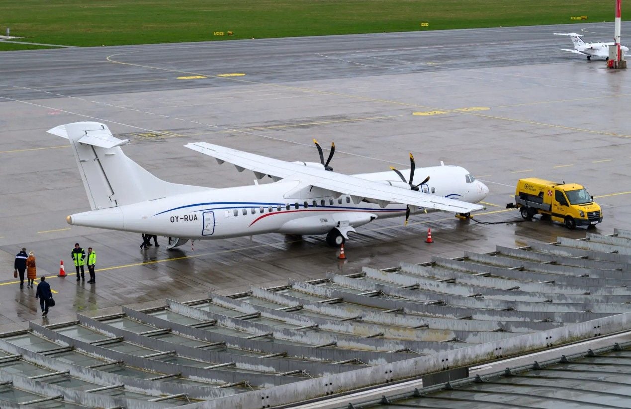 Ein Propellerflugzeug der DAT wird am Flughafen betankt, mehrere Personen stehen daneben.
