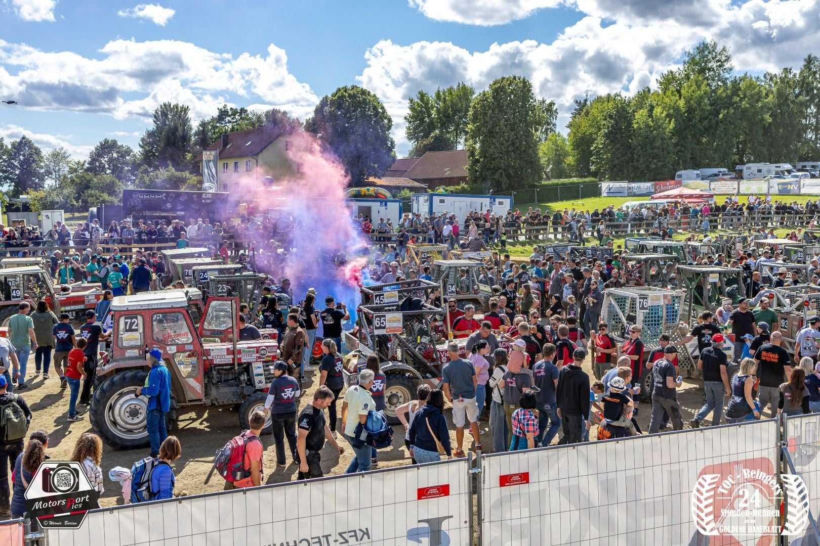 Viele Menschen und Traktoren bei einem Traktorrennen in Reingers, bunter Rauch steigt auf.