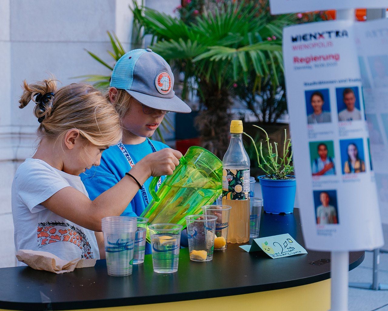 Zwei Kinder bereiten an einem Stand im Wiener Rathaus Limonade mit Zitronenstücken zu.