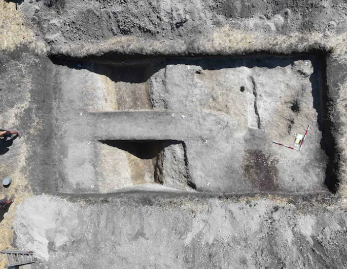 Luftbild einer rechteckigen archäologischen Ausgrabungsstätte mit verschiedenen Gräben im Boden.