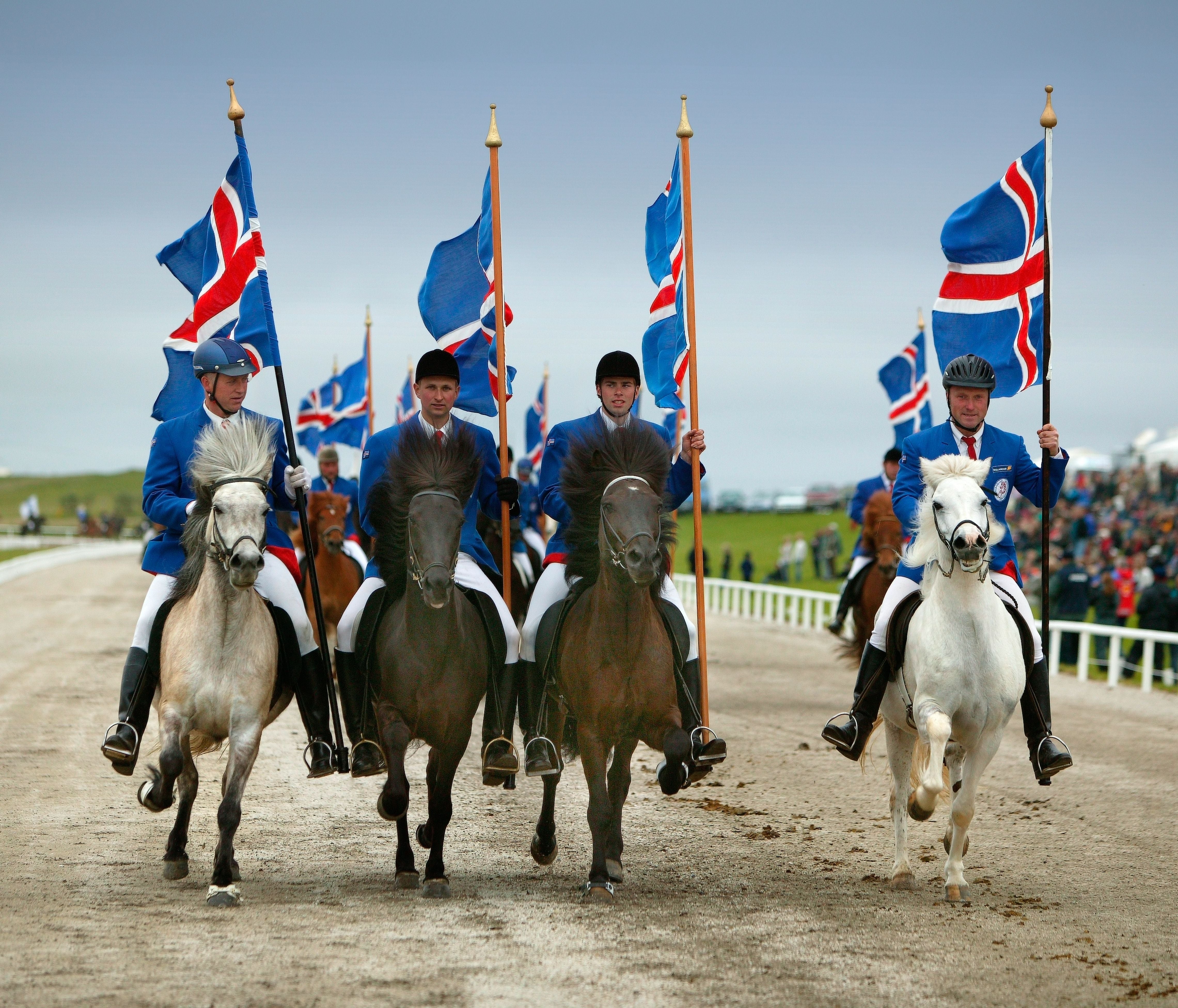 Vier Reiter in blauen Jacken tragen isländische Flaggen bei einer Eröffnungszeremonie.
