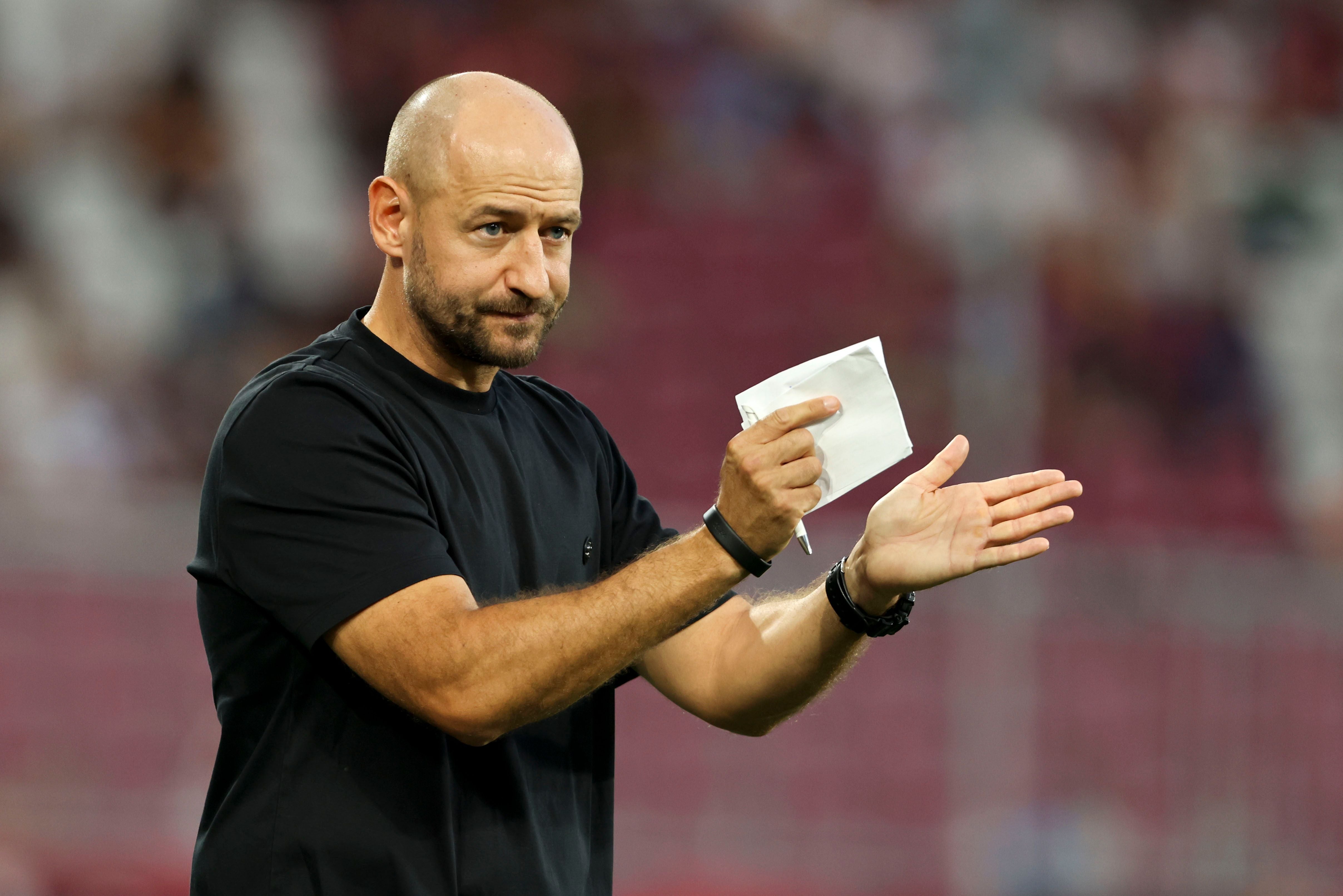 Ein Mann im schwarzen Shirt hält Papier in der Hand und klatscht, unscharfer Hintergrund.
