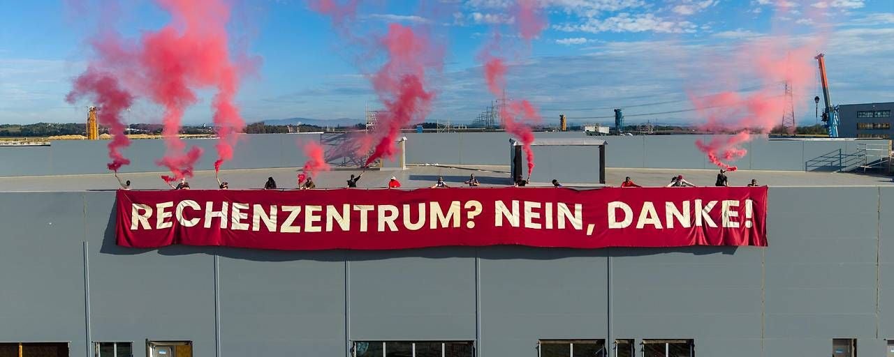 Zwanzig Aktivisten protestieren mit Rauchfackeln und Banner gegen ein geplantes Rechenzentrum.