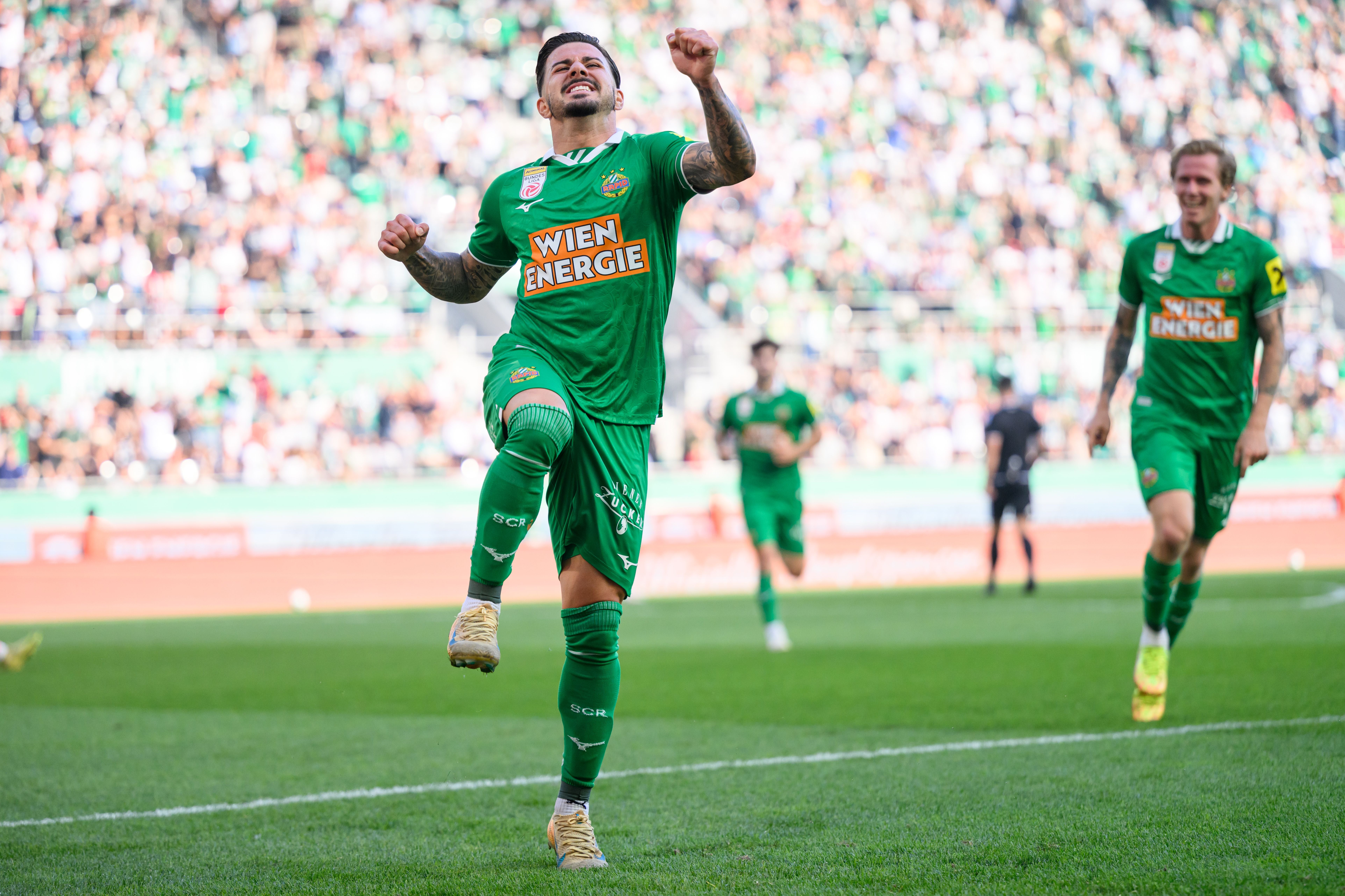 Ein Rapid-Spieler jubelt nach einem Tor im Fußballstadion, Zuschauer jubeln im Hintergrund.