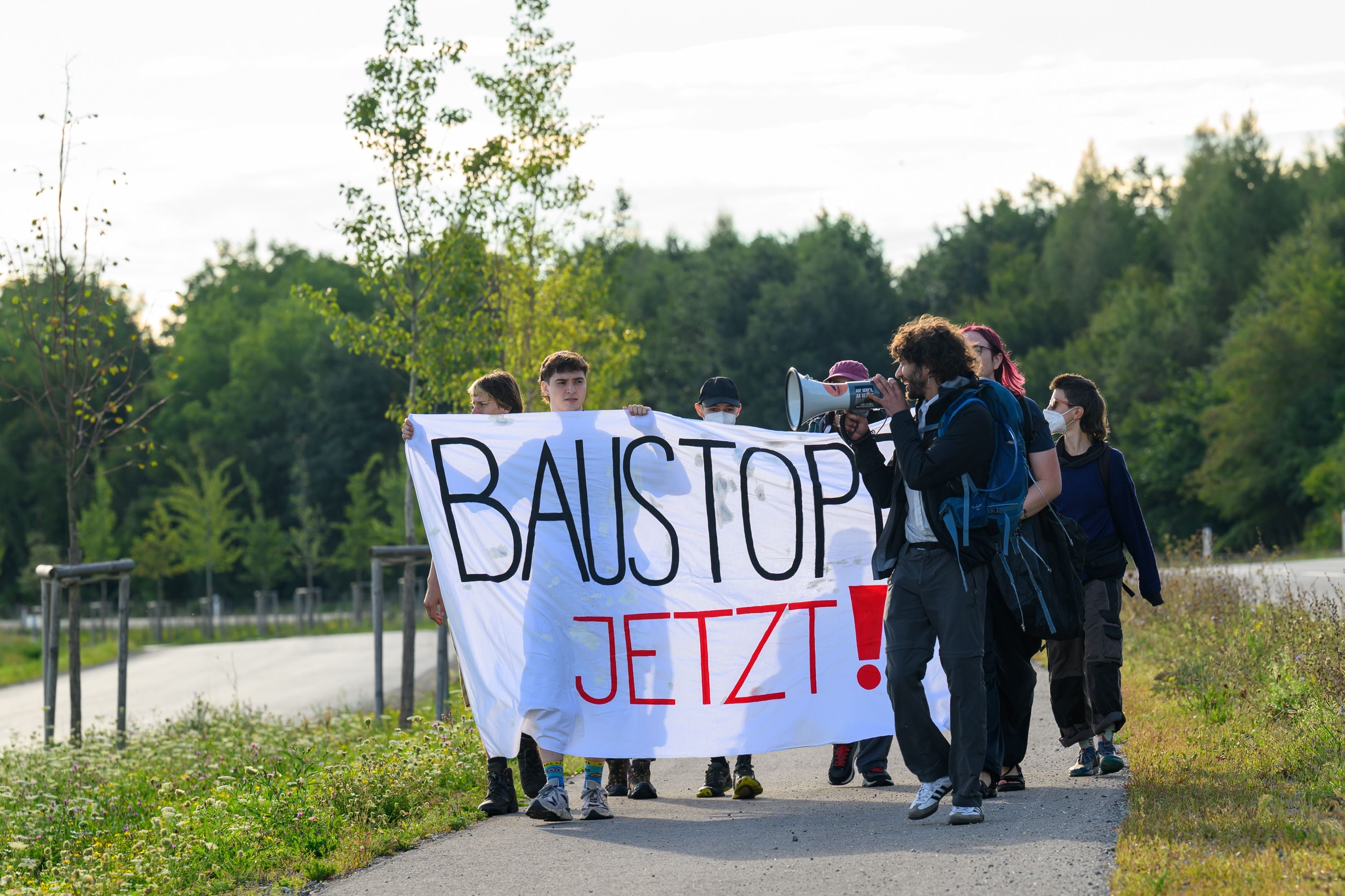 Demonstrierende mit Banner "Baustopp jetzt!" auf einem Weg, Protest gegen ein Bauprojekt.