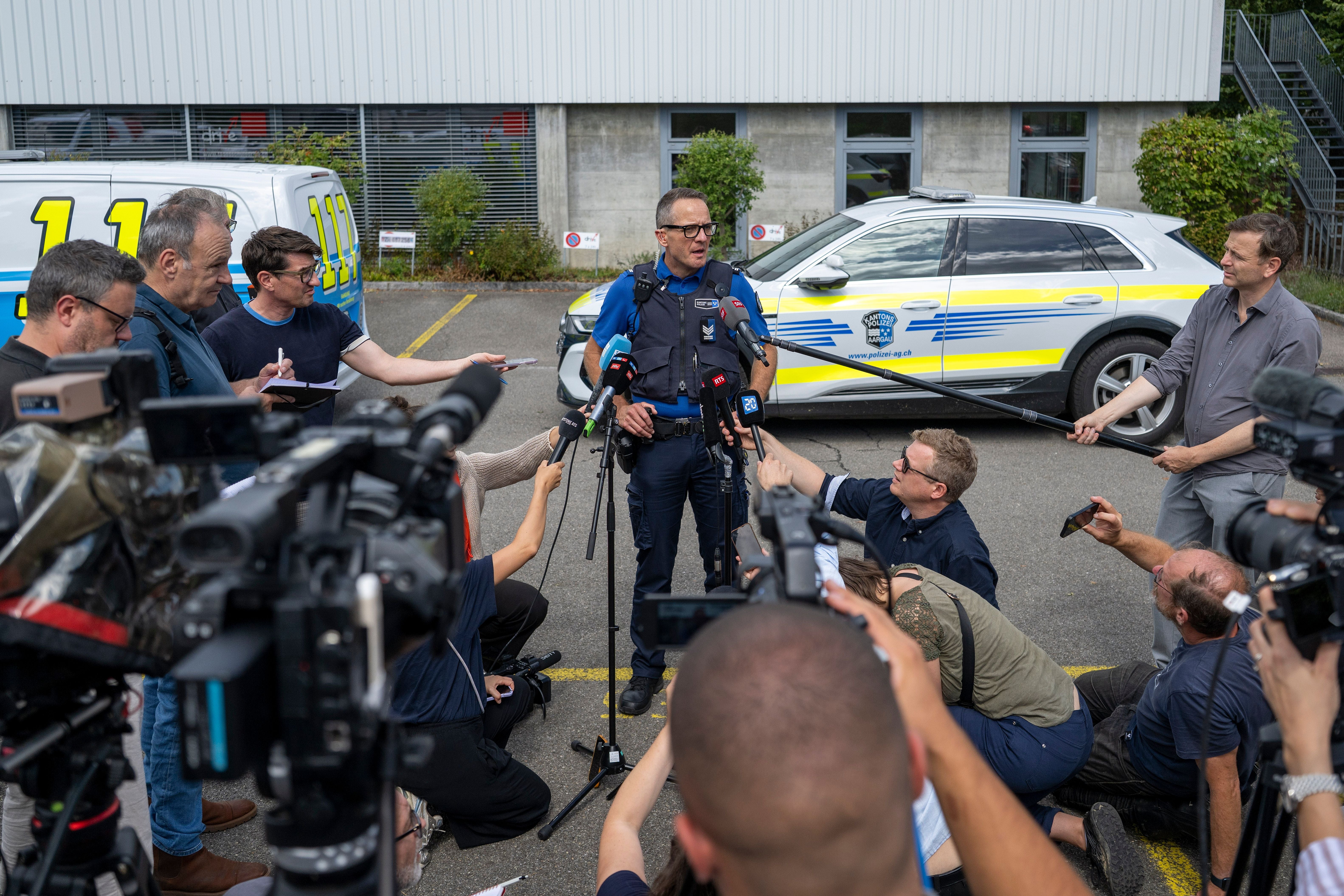 Ein Polizeisprecher informiert Journalisten vor Einsatzfahrzeugen bei einer Pressekonferenz im Freien.