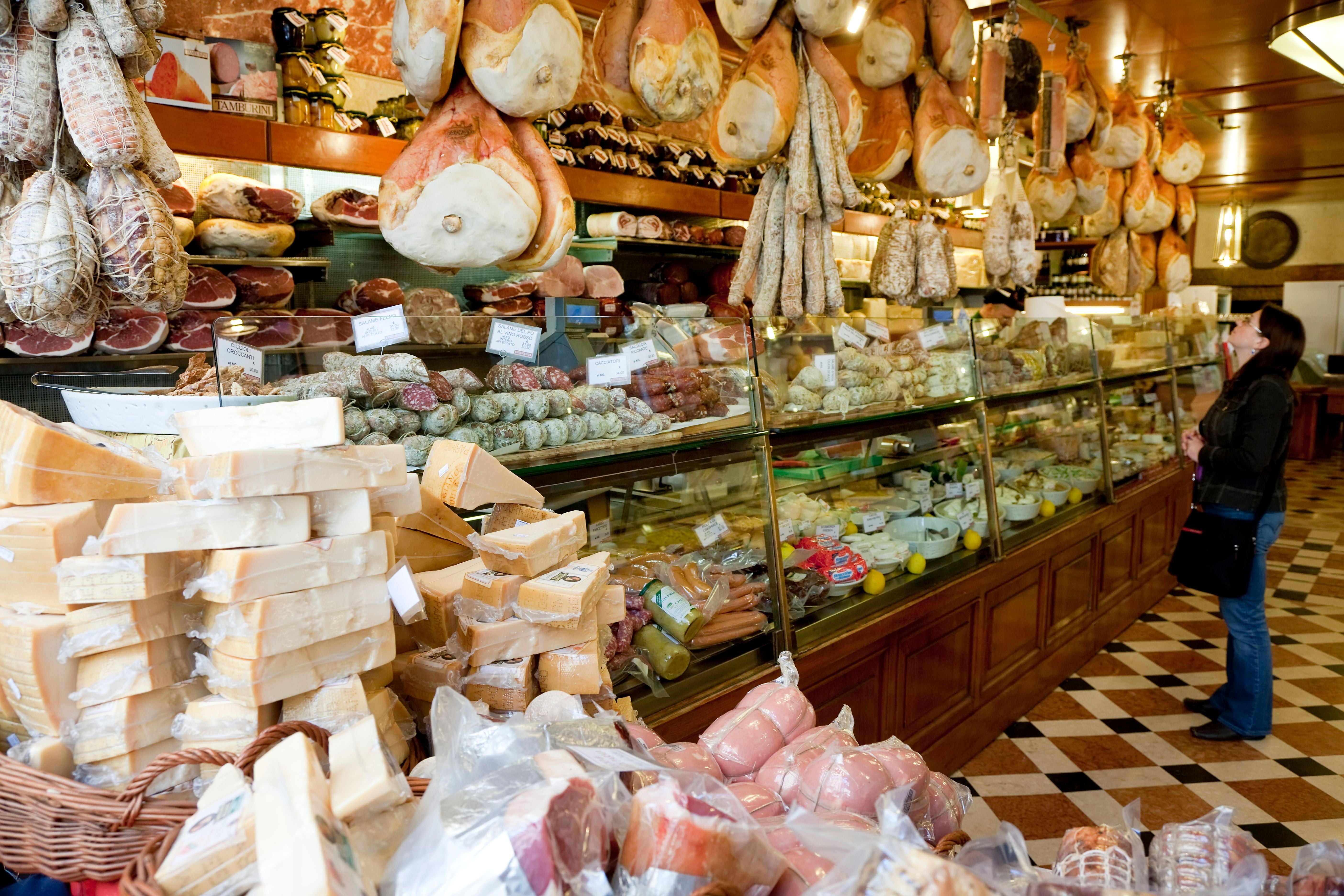 Italienisches Feinkostgeschäft mit Käse, Wurstwaren und Schinken; eine Frau betrachtet die Auslage.