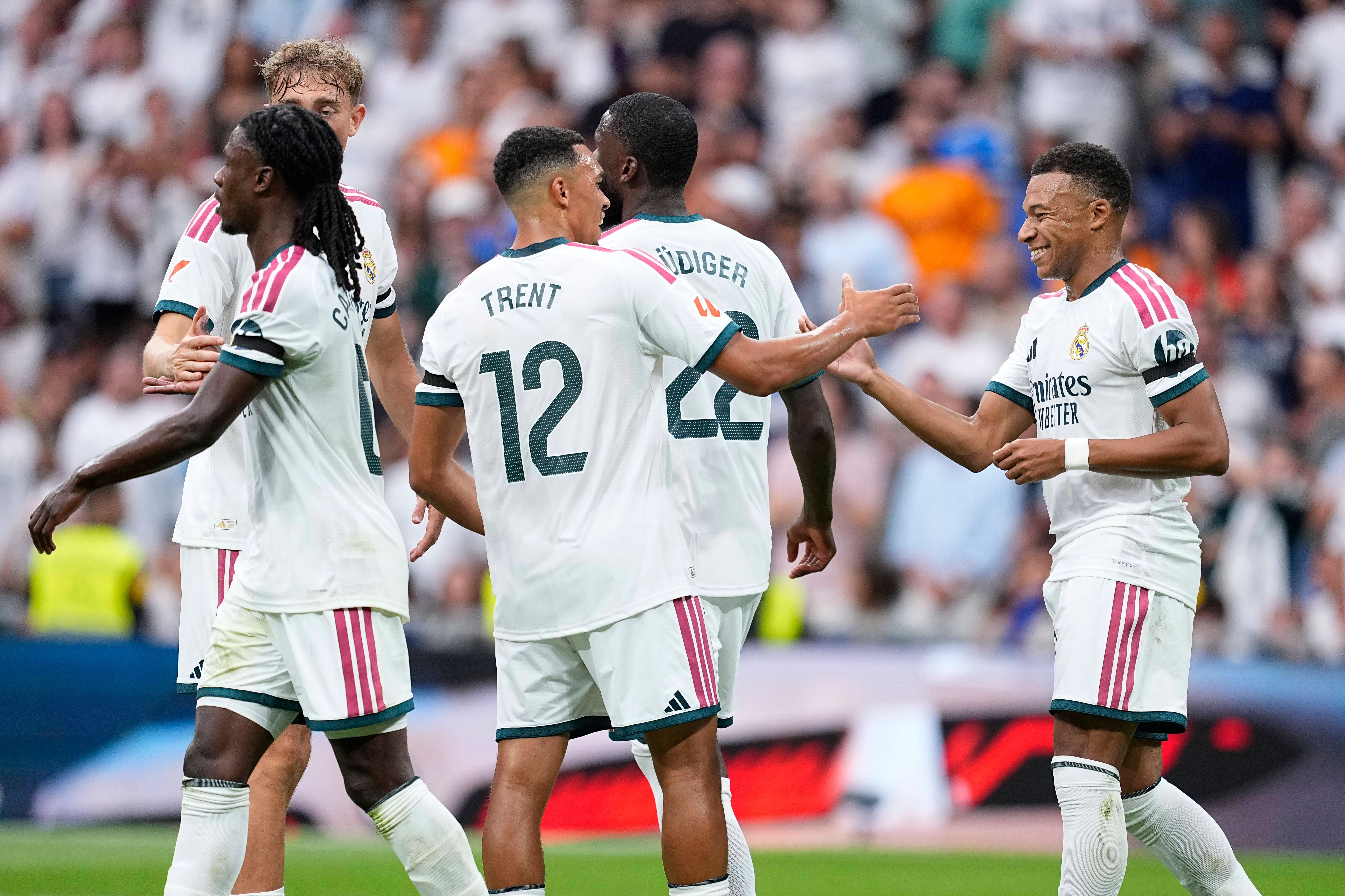 Mehrere Fußballspieler von Real Madrid in weißen Trikots klatschen auf dem Spielfeld ab und jubeln gemeinsam vor vollbesetzten Zuschauerrängen.