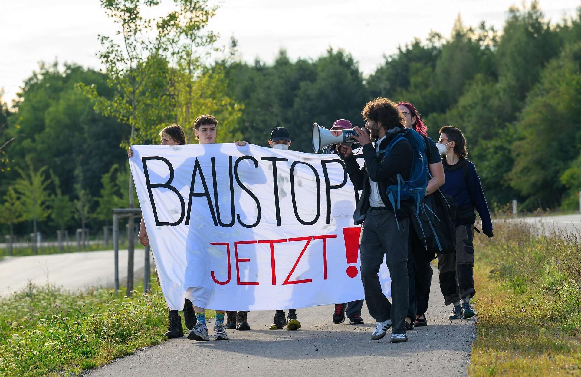 Mehrere Aktivisten halten ein Banner mit der Aufschrift "BAUSTOPP JETZT!" bei einem Protest.