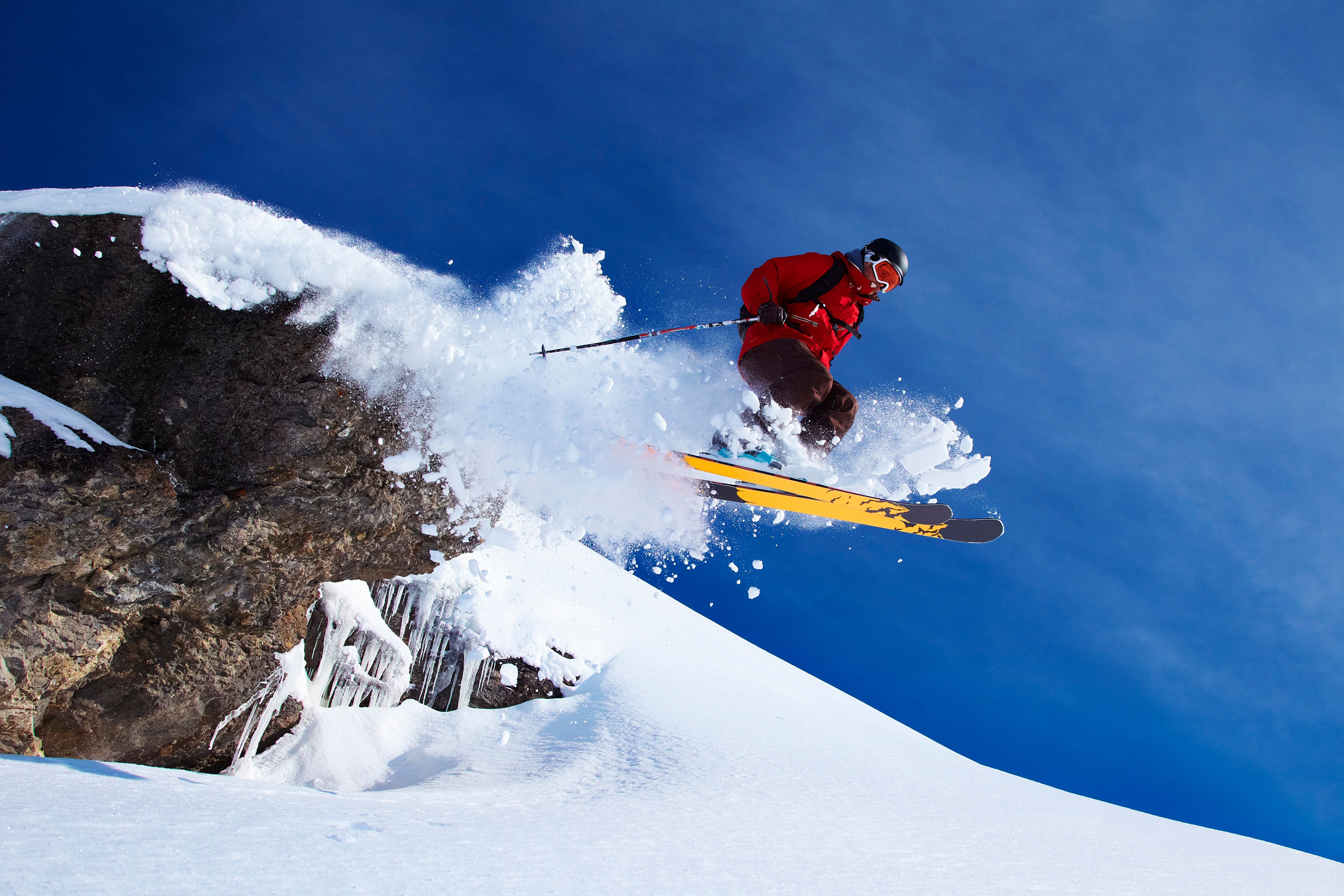 Skifahrer springt über eine mit Schnee bedeckte Klippe vor blauem Himmel.