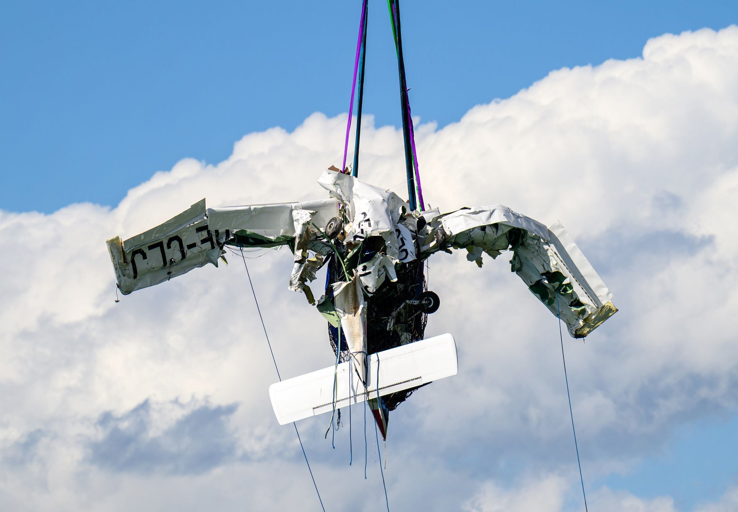 Wrack eines Propellerflugzeugs wird mit Seilen vor wolkigem Himmel aus dem Wasser gehoben.
