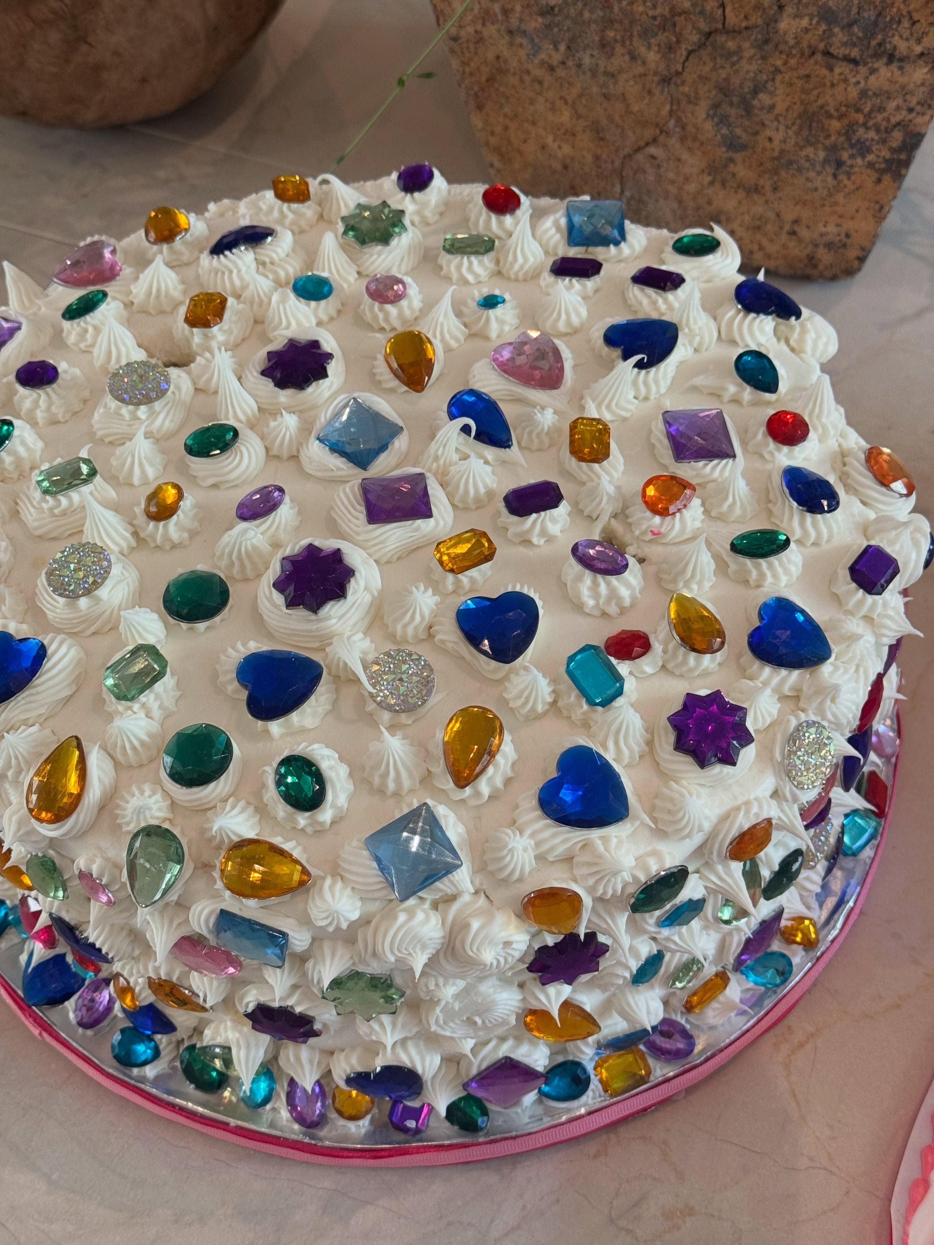 Weiße Torte mit bunten, glitzernden Strasssteinen als Dekoration verziert.